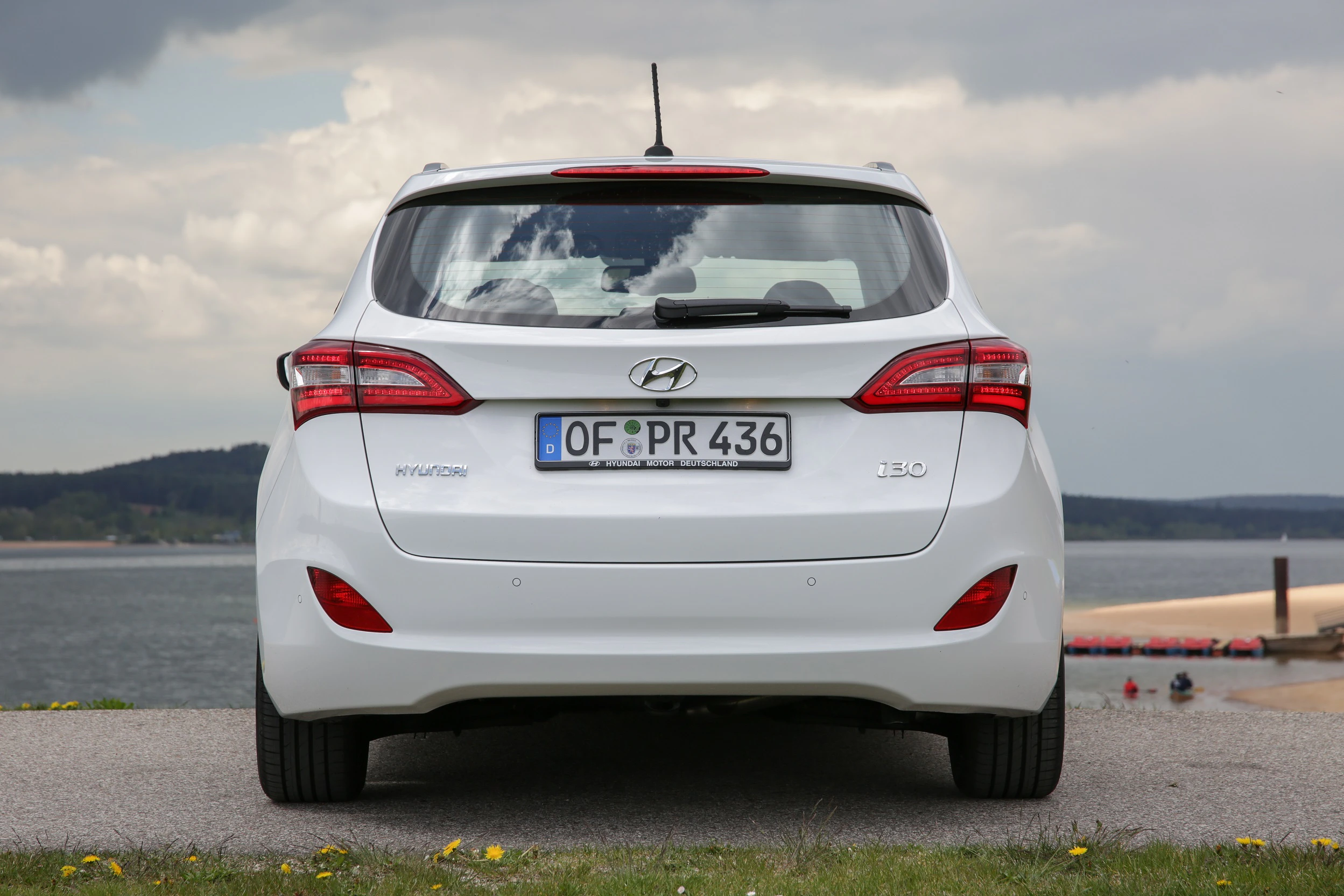 Weißer Hyundai i30 von hinten, geparkt am Ufer eines Sees, bedeckter Himmel im Hintergrund.