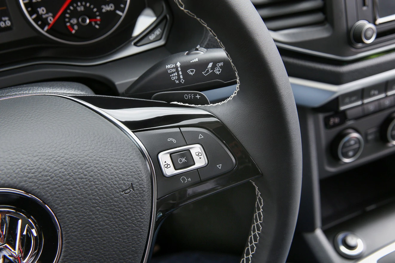 Nahaufnahme eines Autolenkrads mit Multifunktionstasten. Im Hintergrund sind ein Tachometer und Bedienelemente zu sehen.
