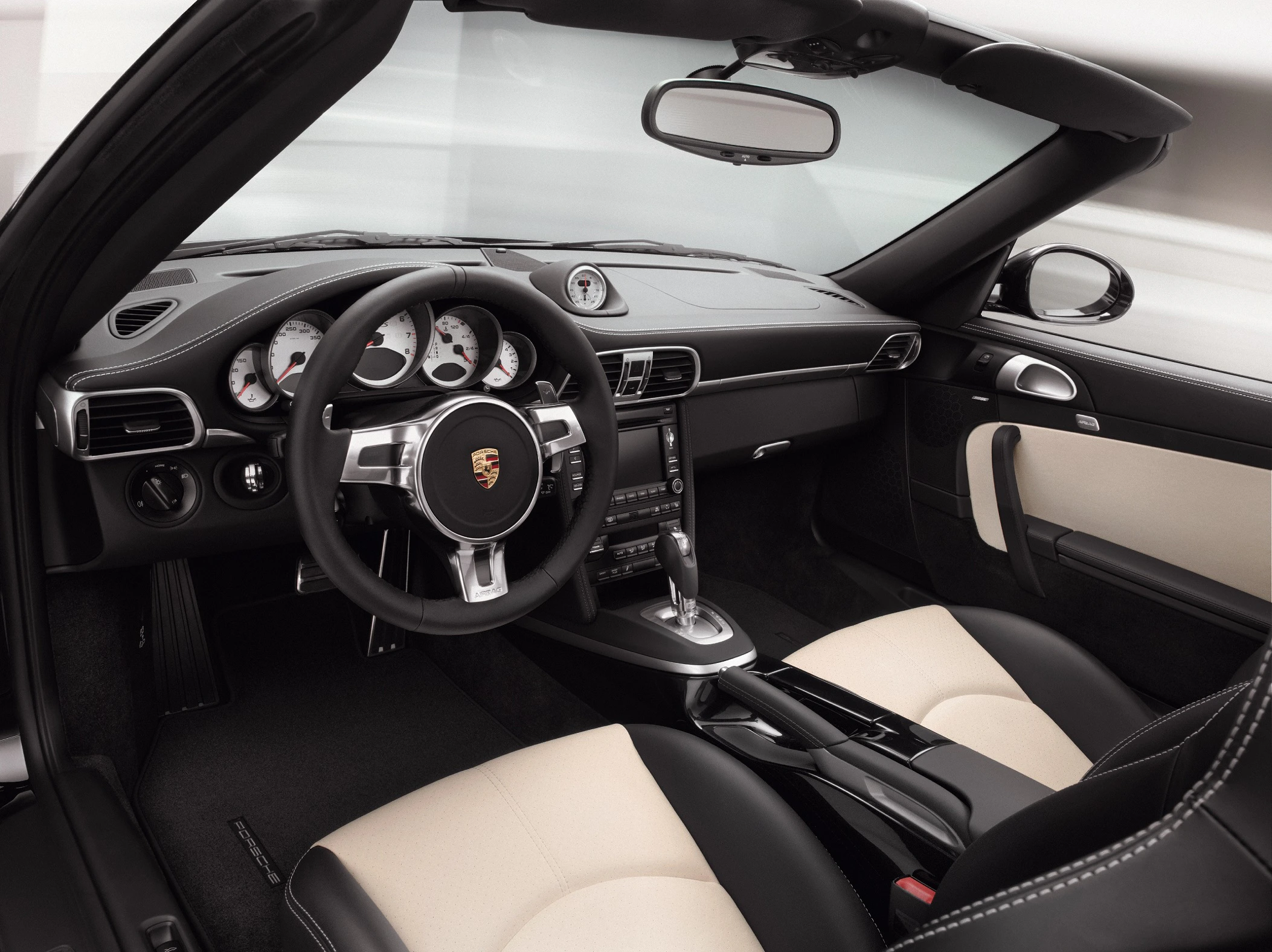 Innenansicht eines luxuriösen Cabriolets mit Lederpolstern, modernem Armaturenbrett und Porsche-Logo auf dem Lenkrad.