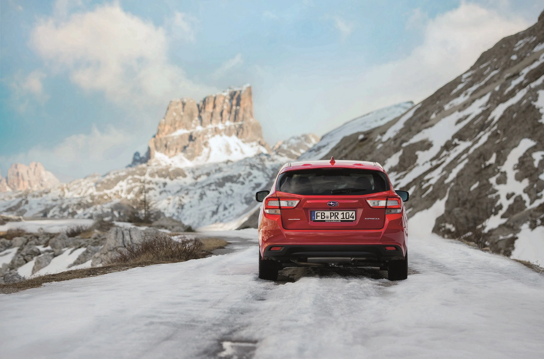 Rotes Auto fährt auf schneebedeckter Straße durch bergige Landschaft bei klarem Himmel.