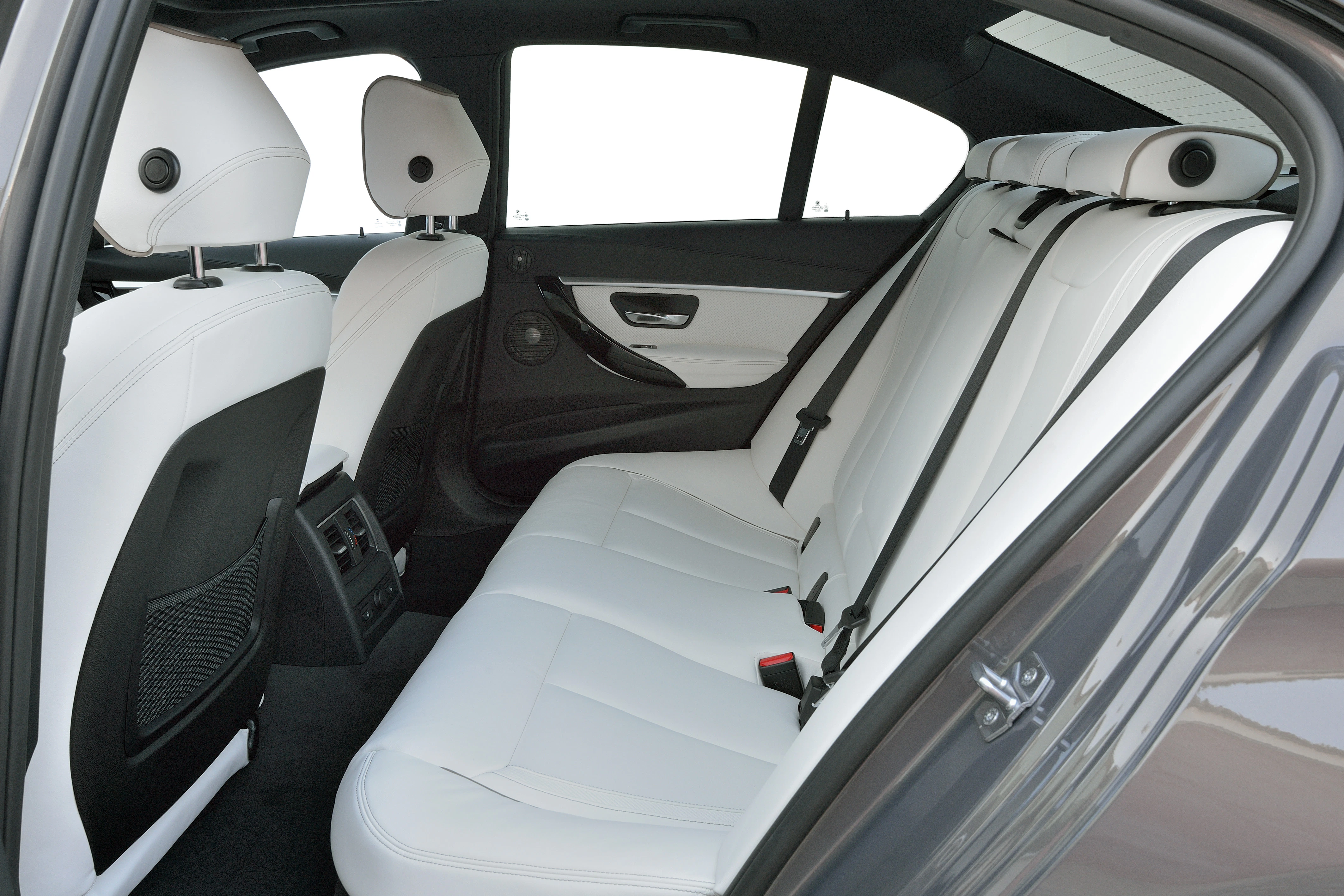 Innenraum eines Autos mit weißen Ledersitzen, Rückbankansicht, helle Kopfstützen und dunkle Türverkleidung.