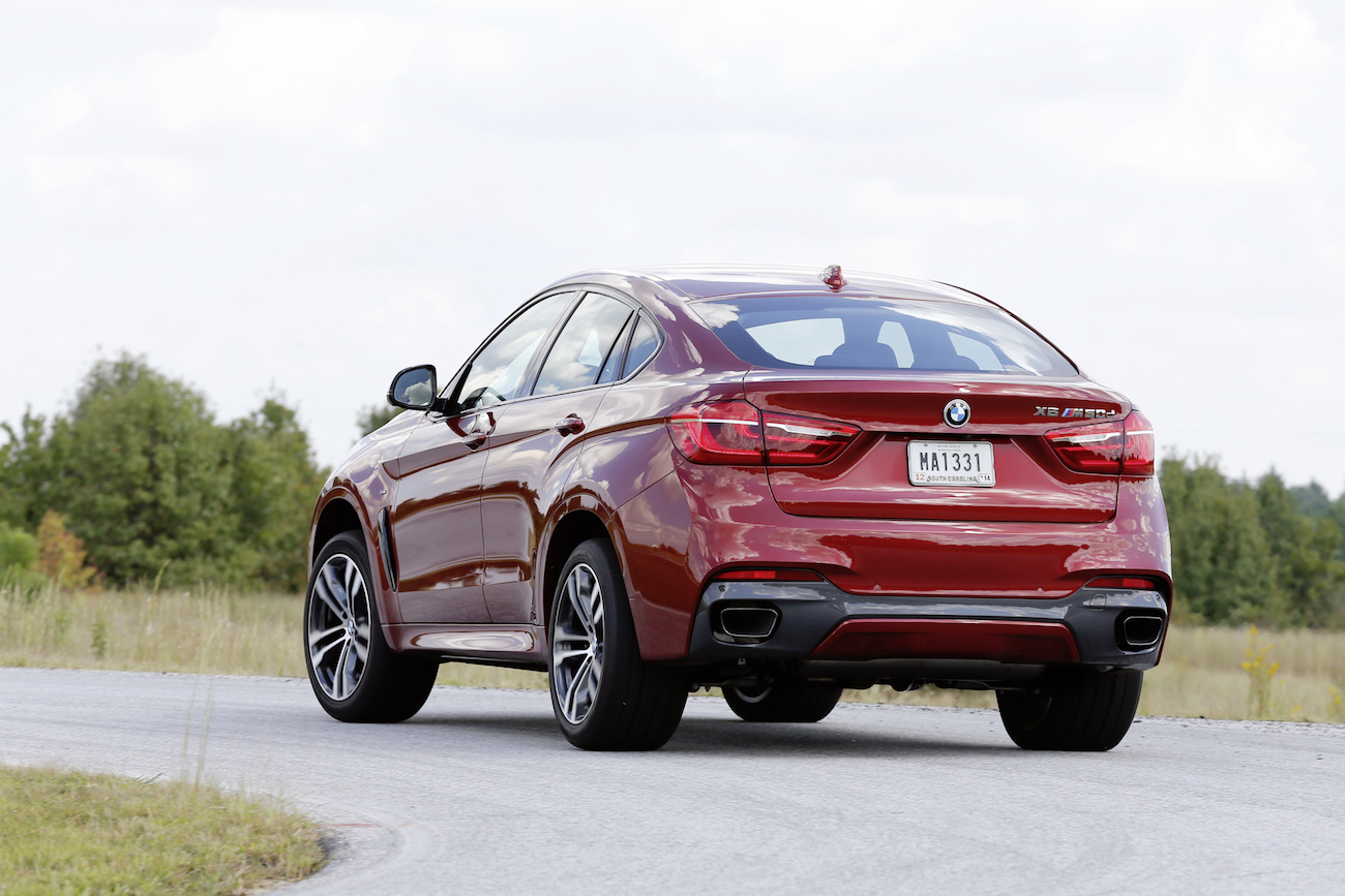 Roter BMW X6 auf einer Landstraße, von hinten fotografiert, umgeben von grüner Landschaft und blauem Himmel.