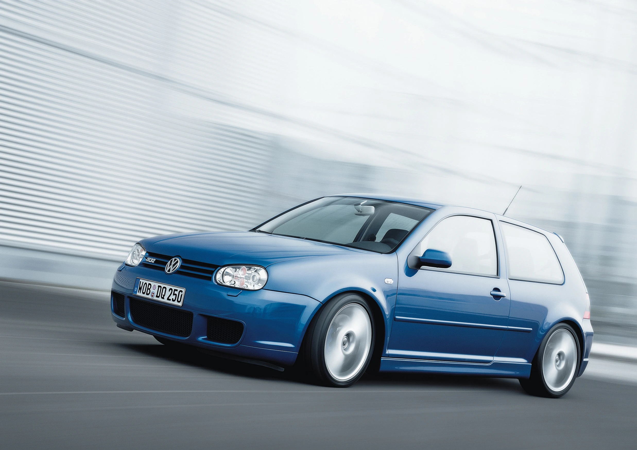 Blauer Volkswagen Golf GTI fährt schnell auf einer Straße, verschwommener Hintergrund zeigt Bewegung.