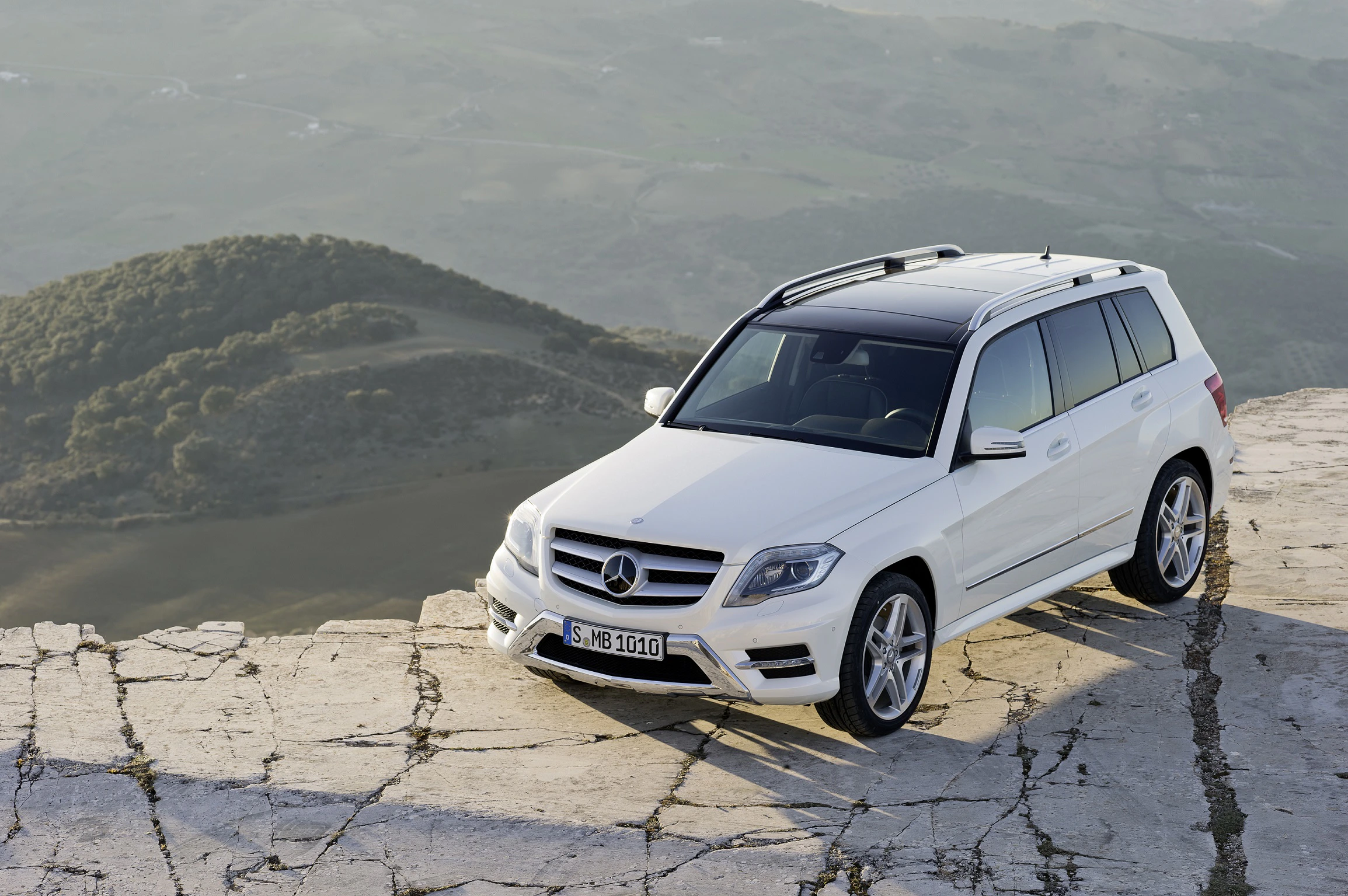 Weißer SUV auf zerklüfteter Klippe mit Blick auf grün bewachsene Hügel im Hintergrund. 