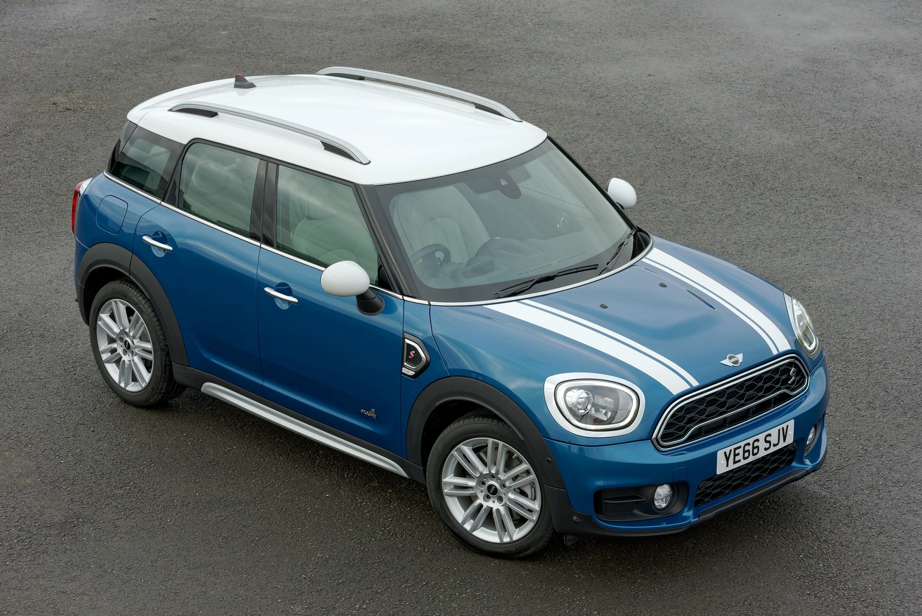 Blauer Mini Cooper mit weißen Streifen und Dach, parkend auf Asphalt. Fünf Türen, sportliches Design, silberne Felgen.