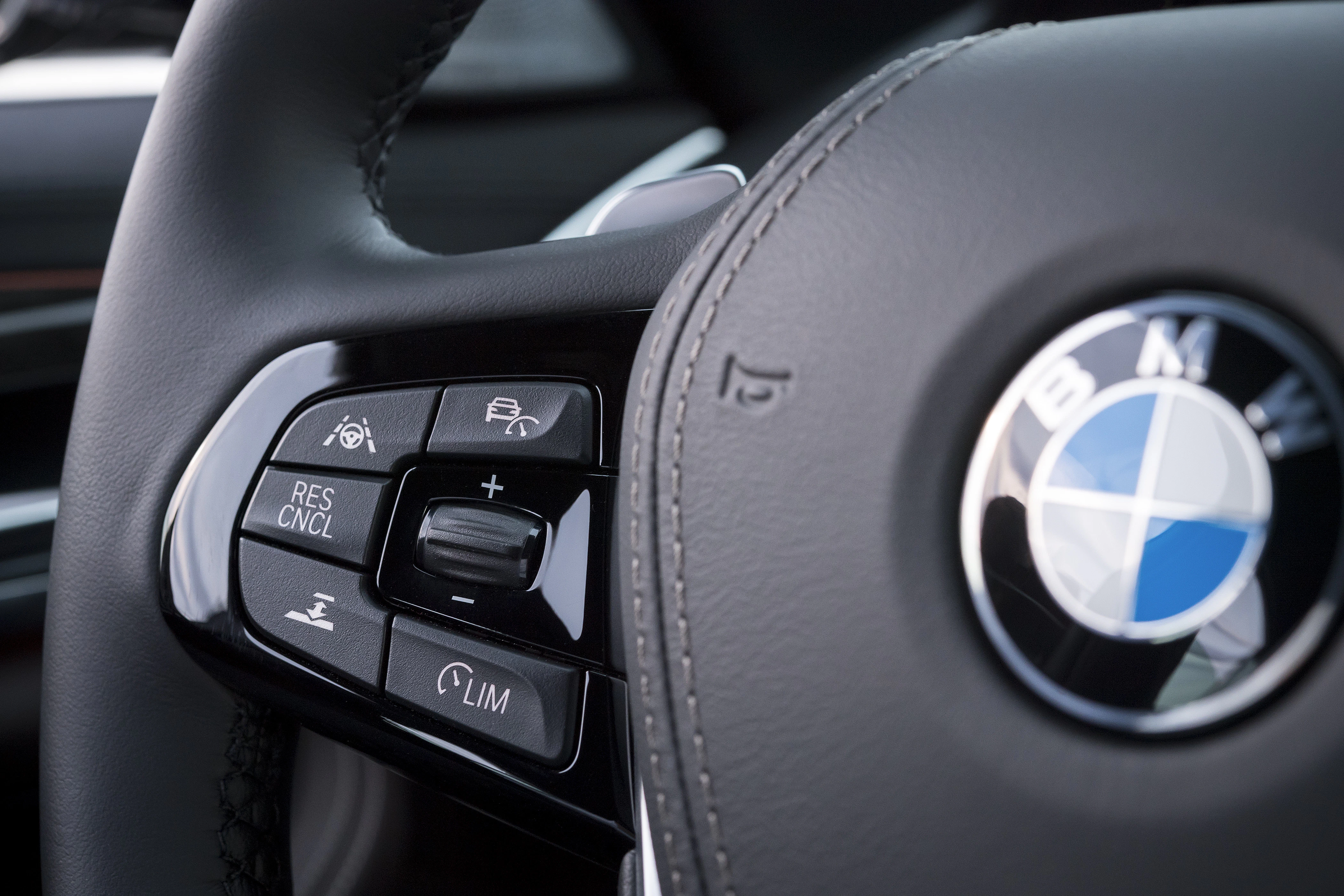 Nahaufnahme eines BMW-Lenkrads mit verschiedenen Bedientasten wie Tempomat- und Lautstärkeregler.