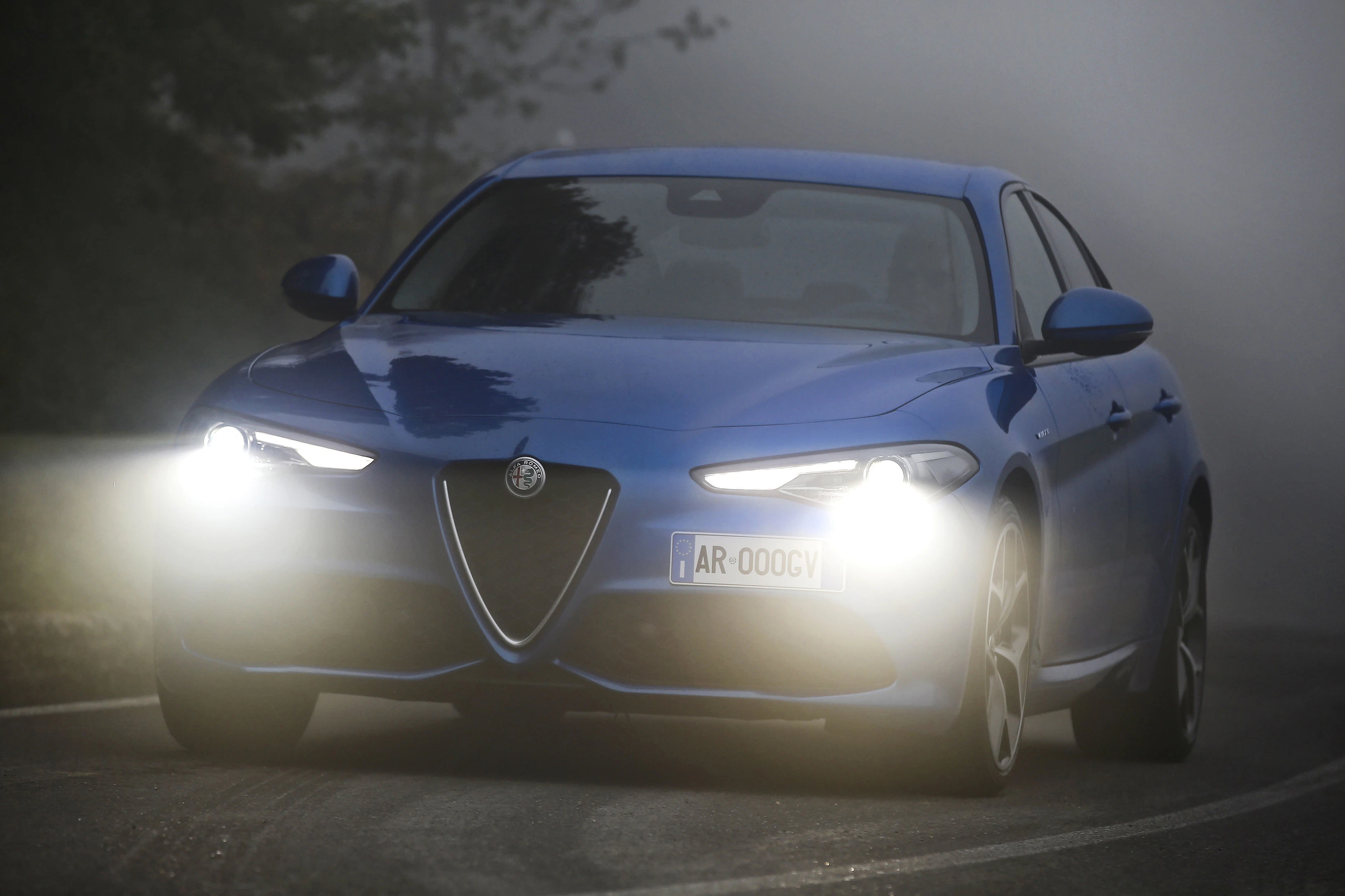 Blaues Auto mit eingeschalteten Scheinwerfern fährt bei Nebel auf einer nassen Straße.