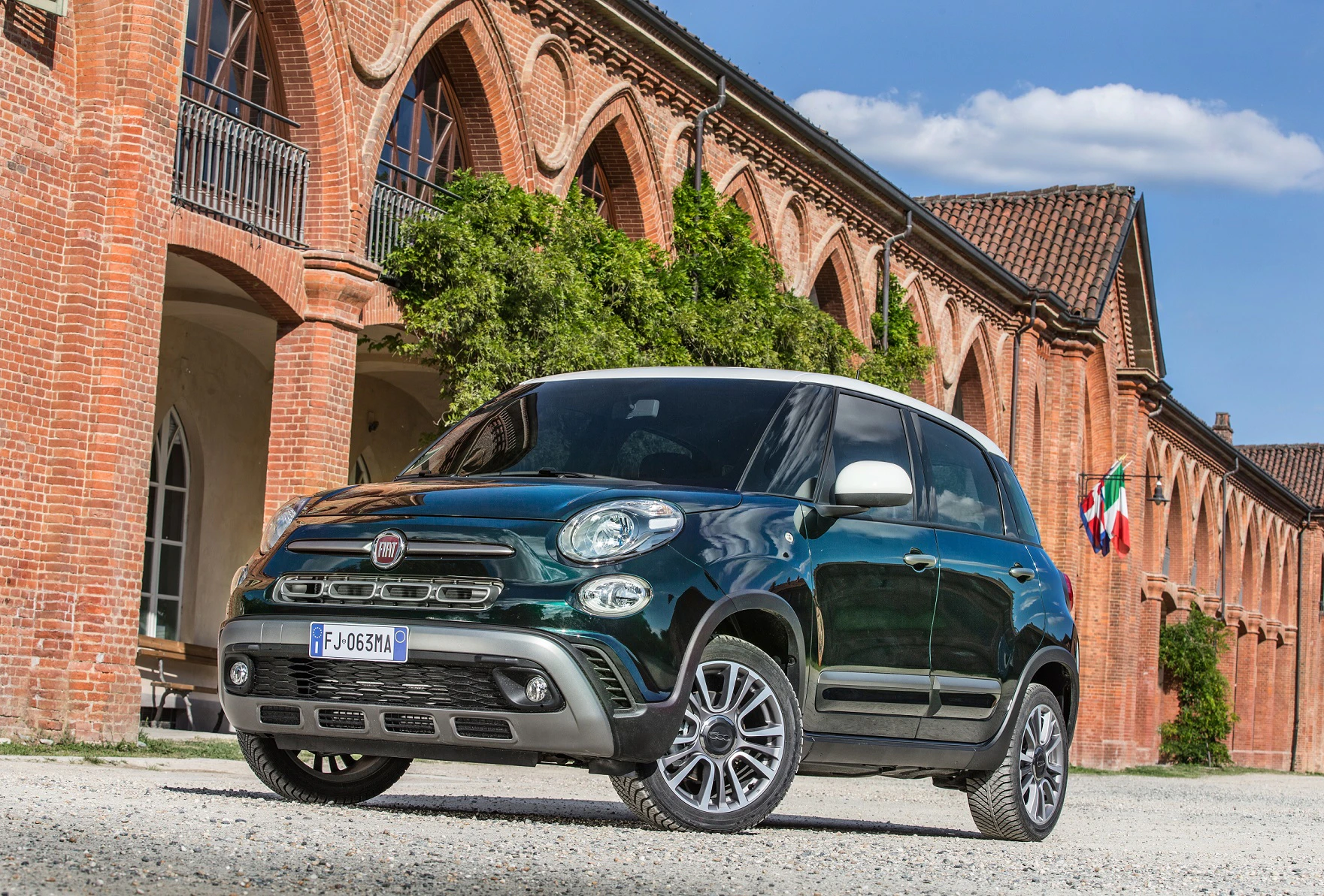 Grüner SUV parkt vor einem alten Backsteingebäude mit Bögen und italienischer Flagge, sonniger Tag.