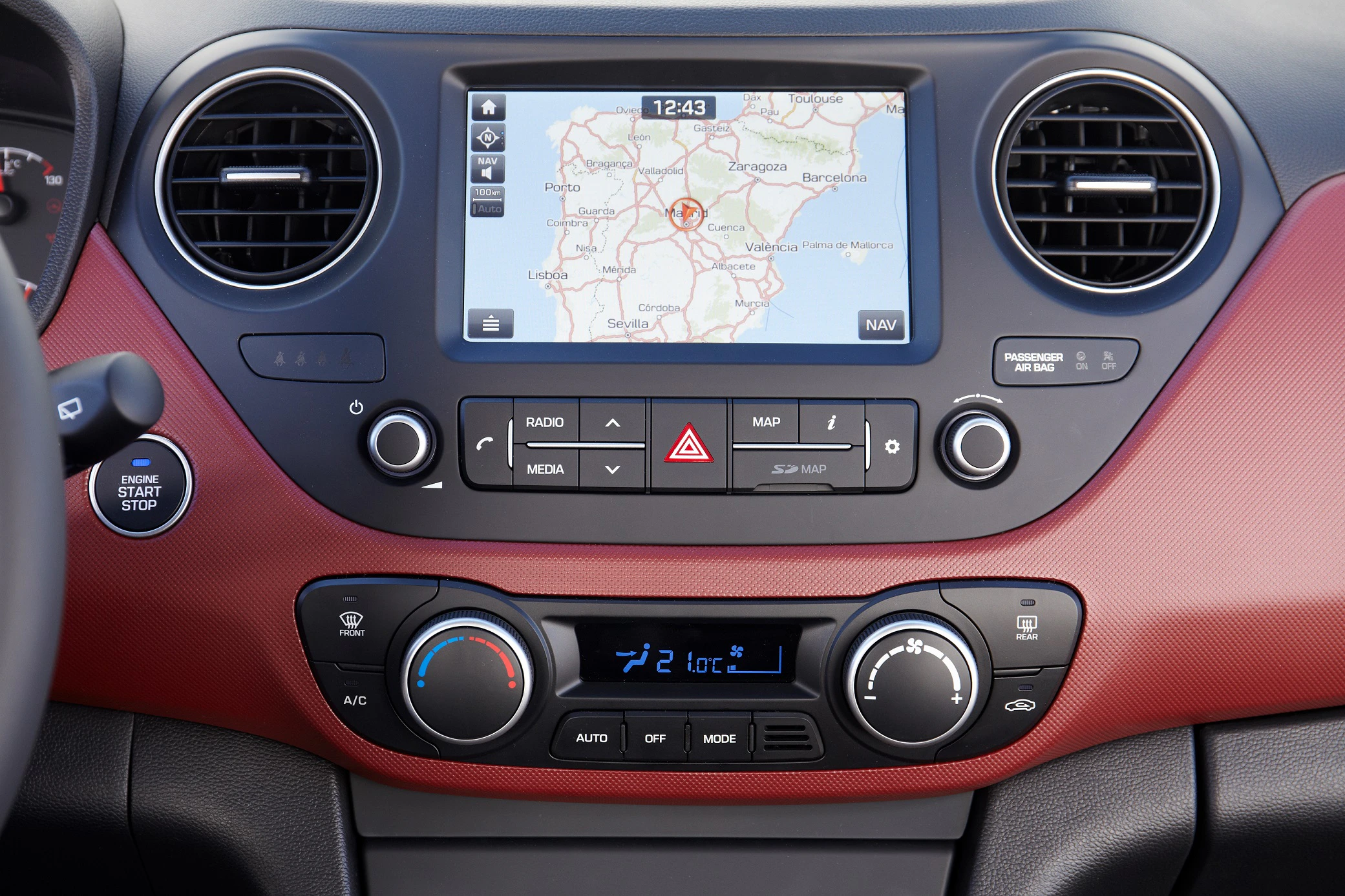 Anzeige eines Autonavigationssystems mit Straßenkarte auf dem Bildschirm, umgeben von Lüftungsschlitzen und Bedienelementen für Radio und Klimaanlage.