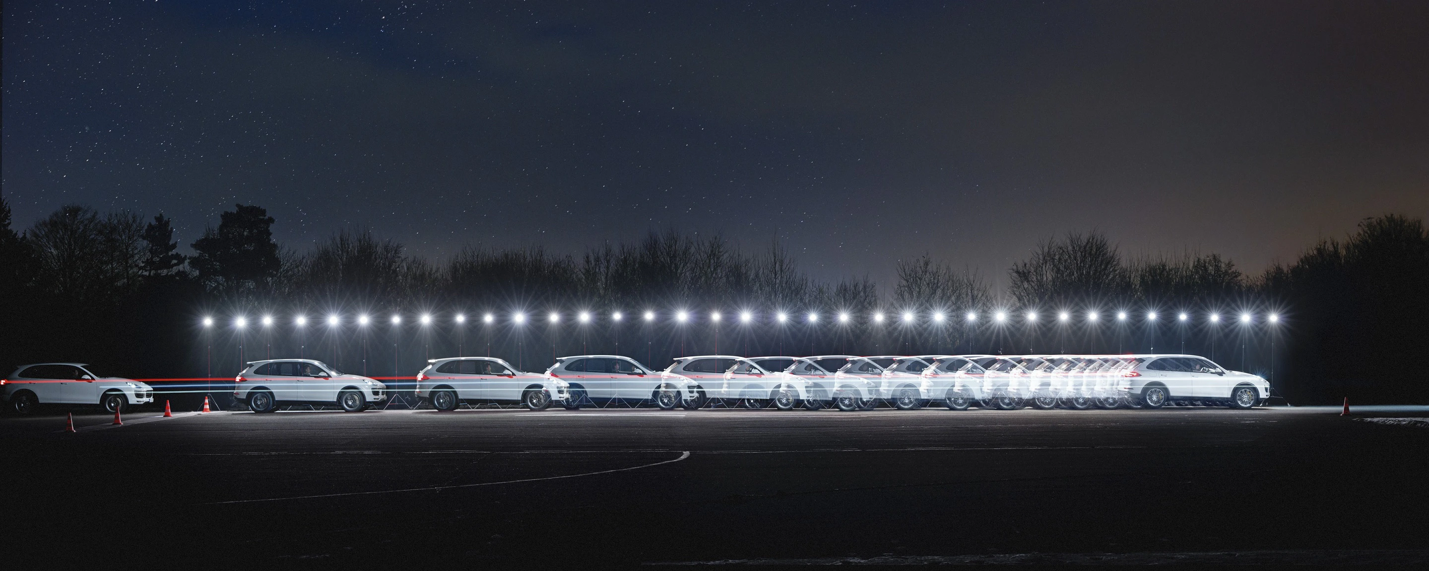 Nachtaufnahme eines weißen Autos mit Lichtspuren, die seine Bewegung auf einem dunklen, bewaldeten Hintergrund darstellen.