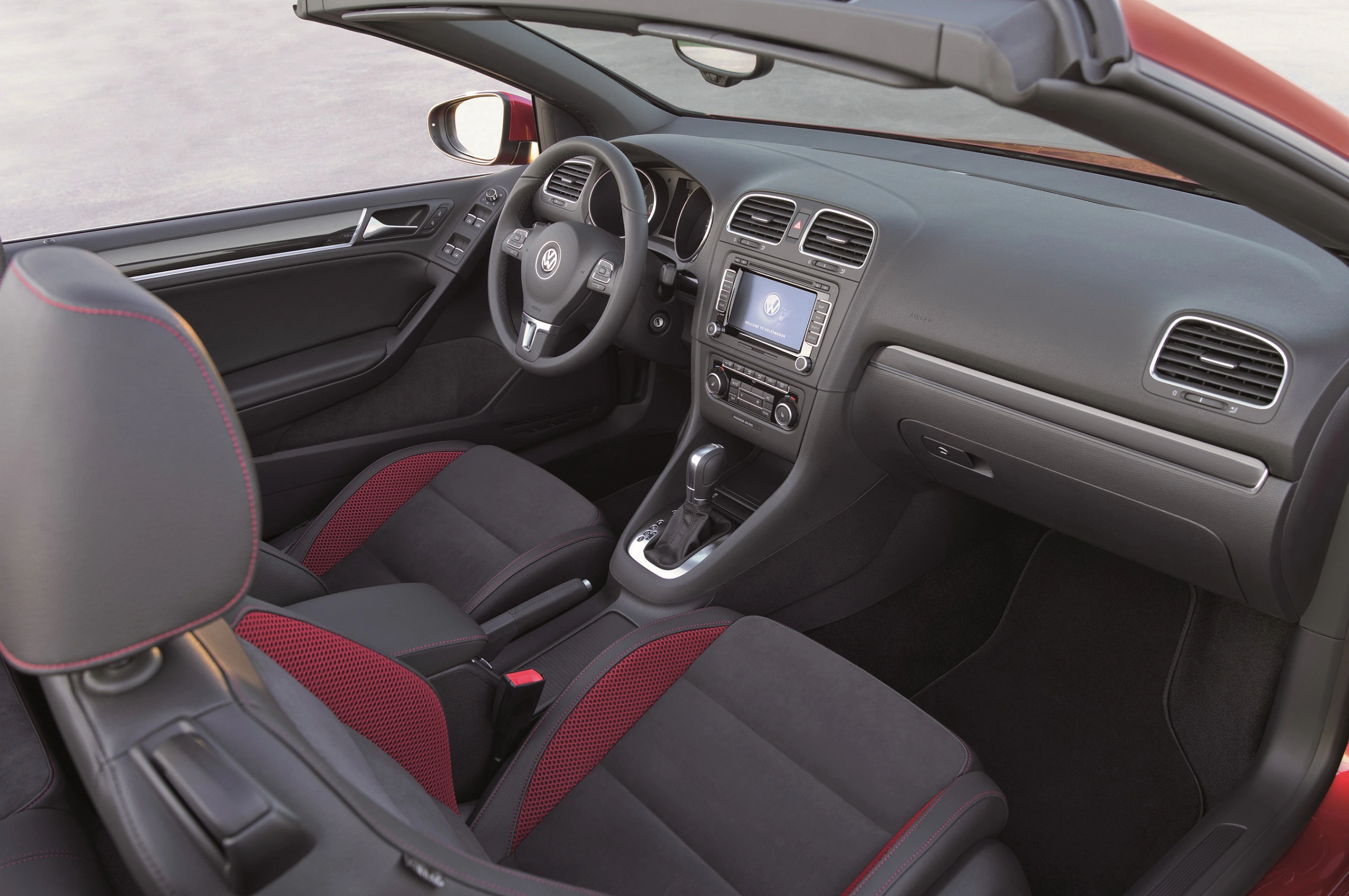 Innenraum eines modernen, offenen Cabriolets mit schwarzen und roten Sitzen, einem zentralen Bildschirm und einem Automatik-Schaltknüppel.