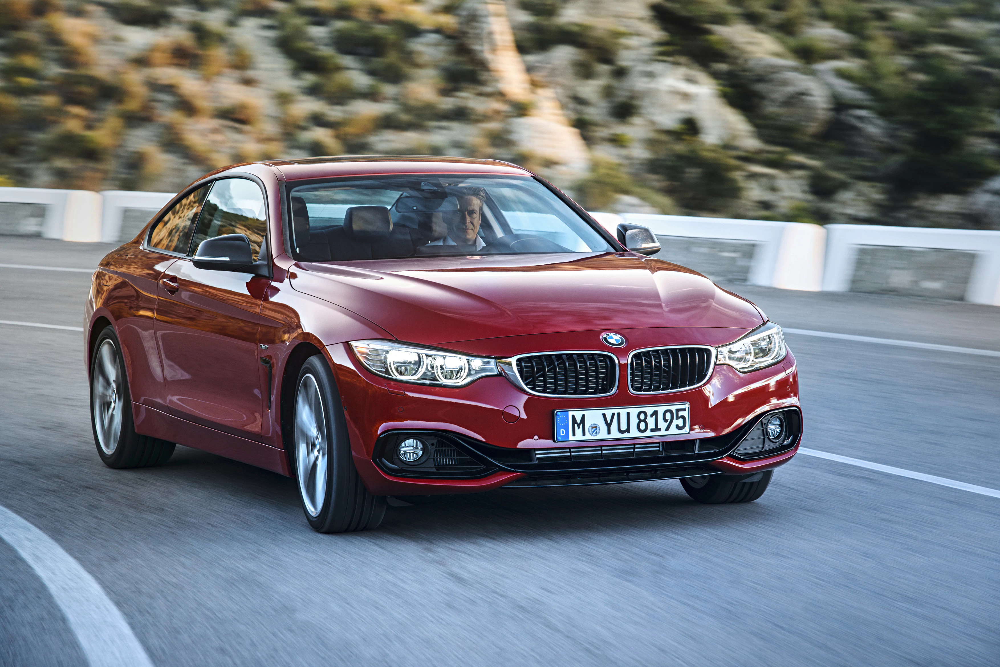 Roter BMW fährt auf einer kurvigen Bergstraße bei Tageslicht. Dynamisches Fahrerlebnis im Vordergrund.