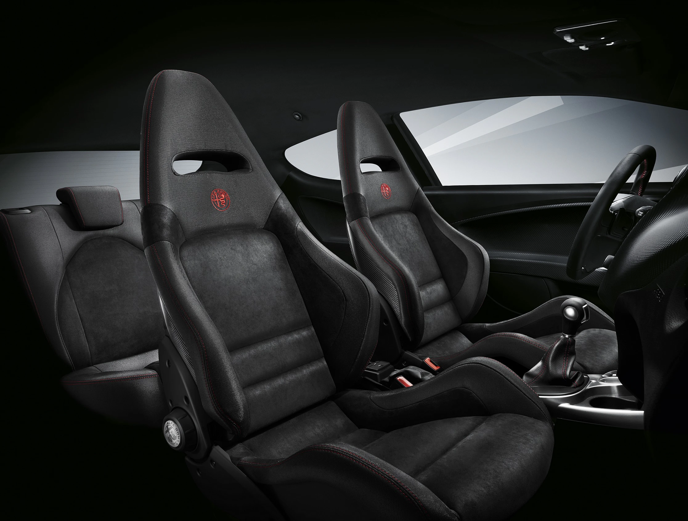 Innenraum eines sportlichen Autos mit zwei schwarzen, ergonomischen Sitzen, roten Logo-Details und einem modernen Armaturenbrett.