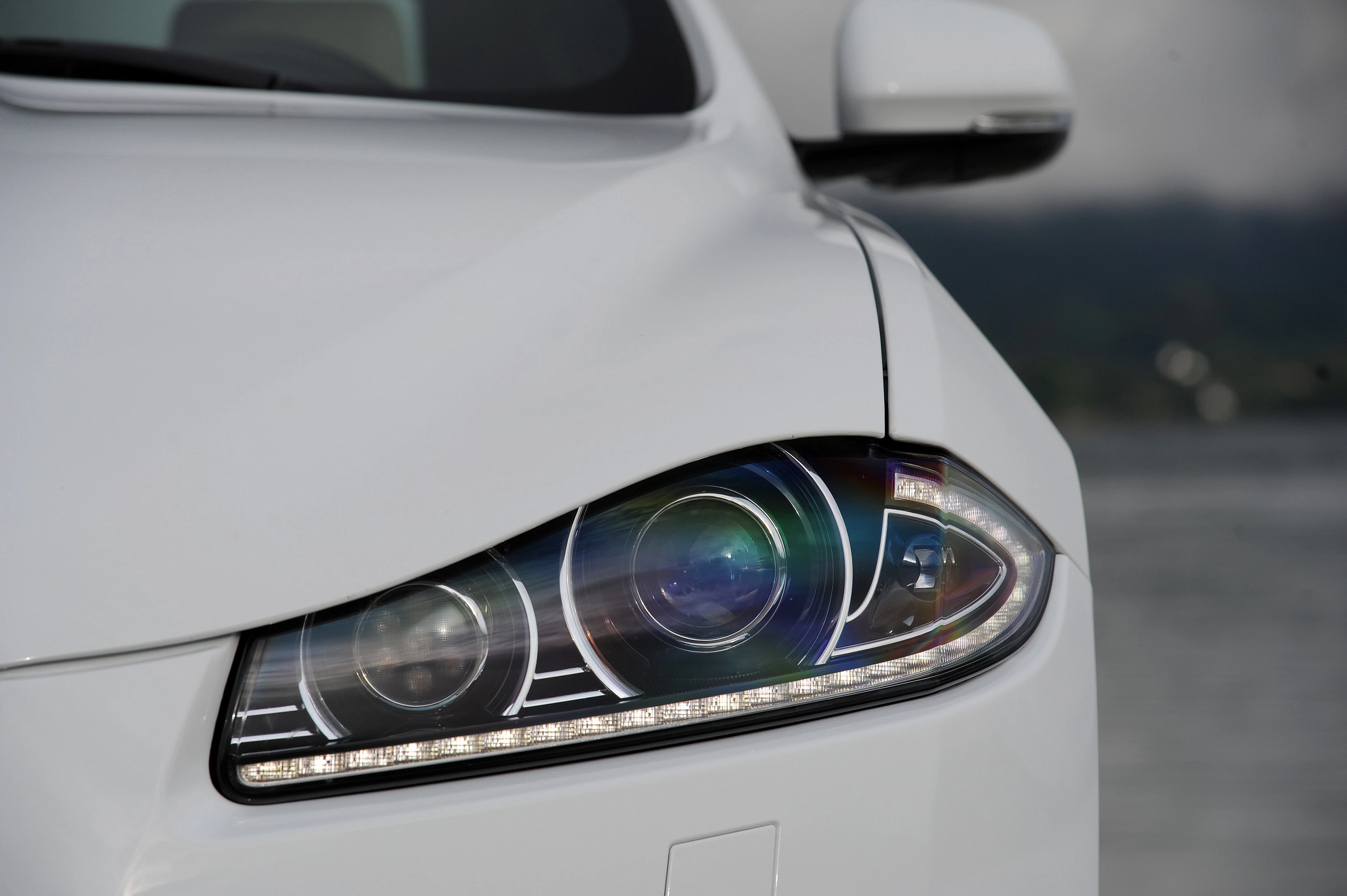 Nahaufnahme eines weißen Autoscheinwerfers mit modernem Design und LED-Leuchten, im Hintergrund verschwommene Landschaft.
