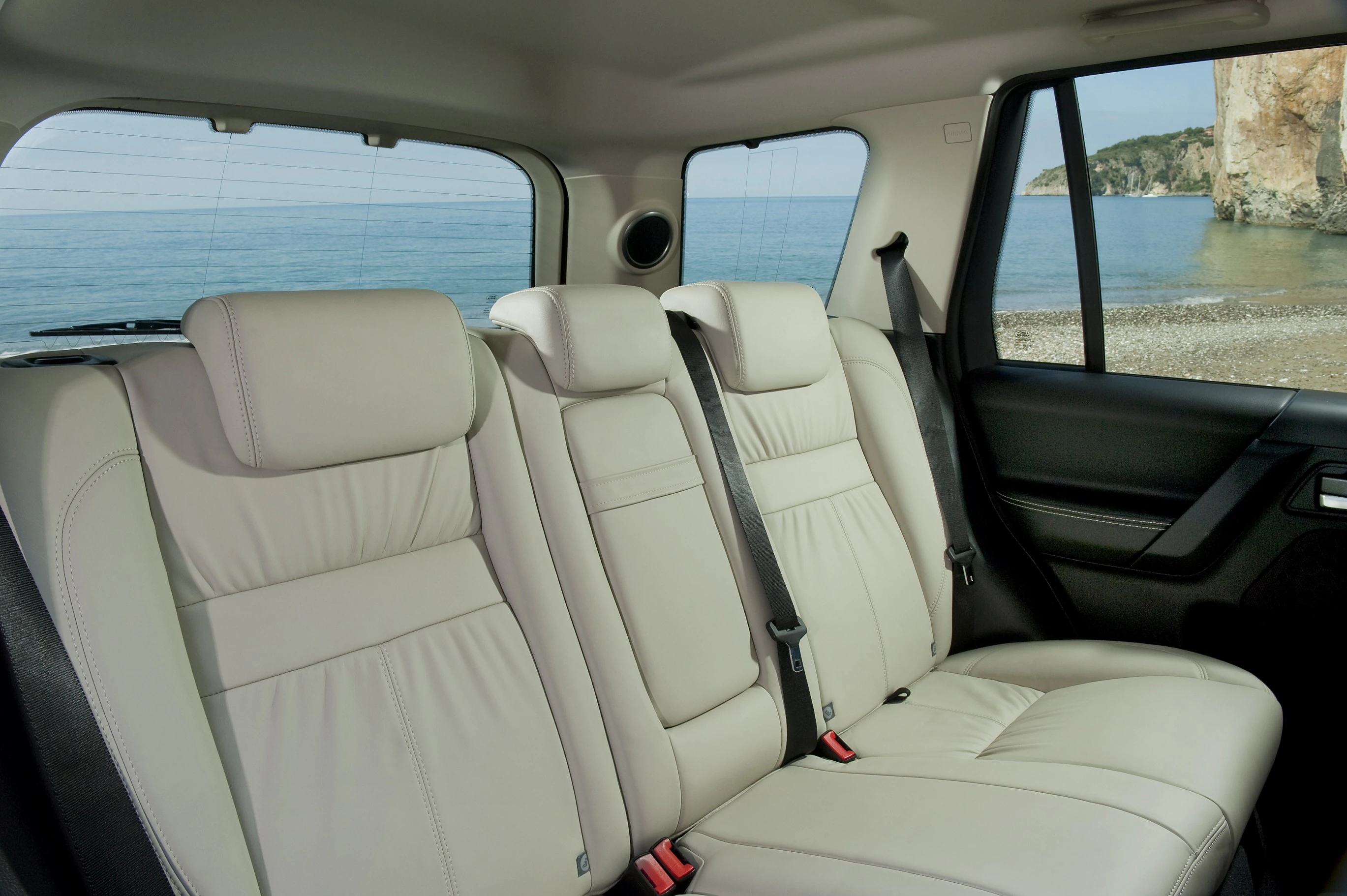 Innenraum eines Autos mit beigen Ledersitzen und Blick auf das Meer durch die Fenster. Im Hintergrund Felsen und Küstenlandschaft.