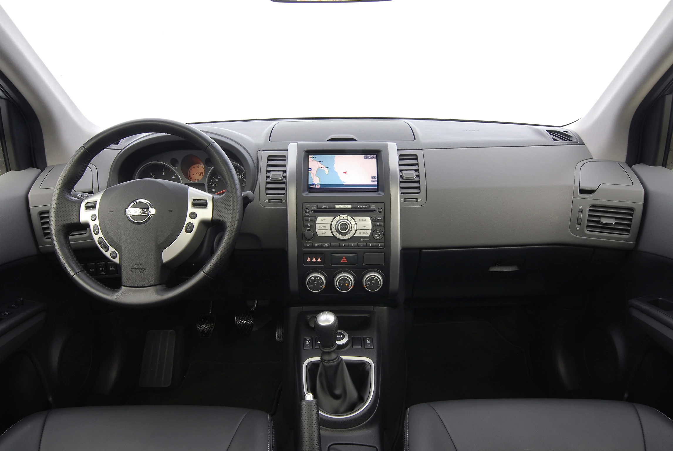 Innenraum eines Autos mit zentralem Touchscreen, Lenkrad links, manueller Gangschaltung, Lüftungsschlitzen und schwarzen Ledersitzen.