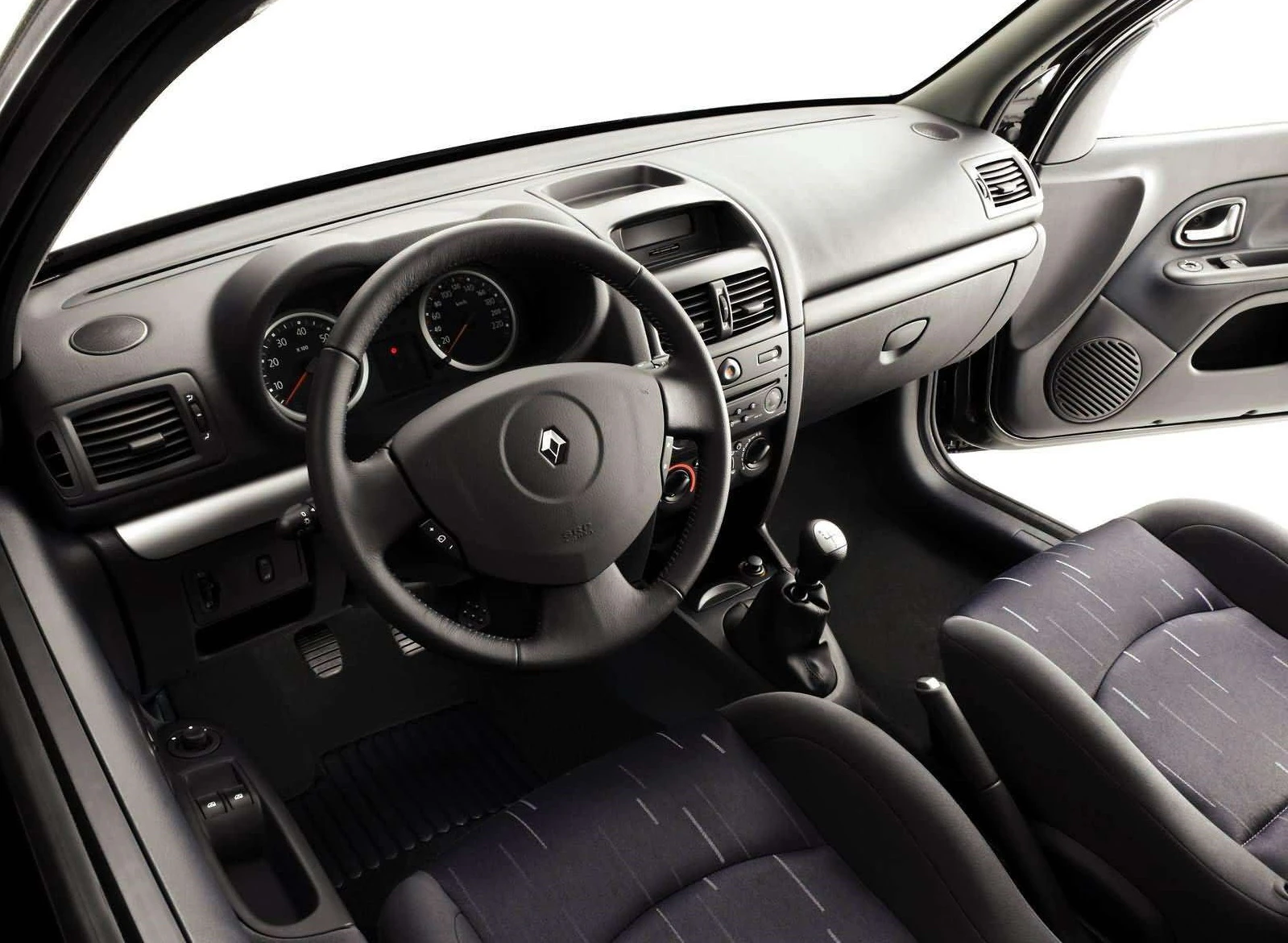 Das Bild zeigt das Innere eines Autos mit einem Lenkrad, Schalthebel und Armaturenbrett. Die Sitze sind schwarz und grau gestreift.