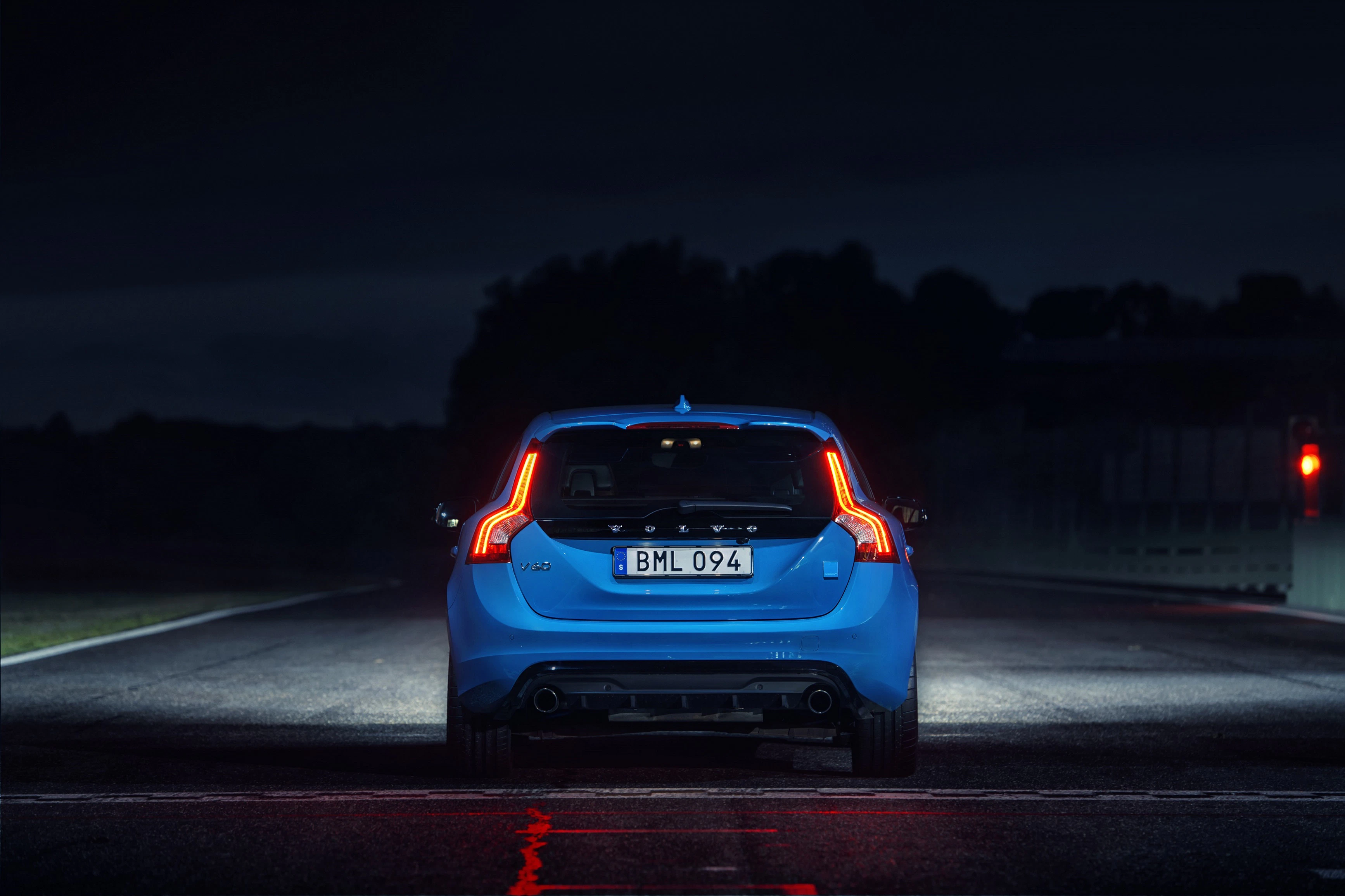 Blaues Auto von hinten bei Nacht auf einer Rennstrecke mit leuchtenden Rücklichtern und verschwommener Umgebung.