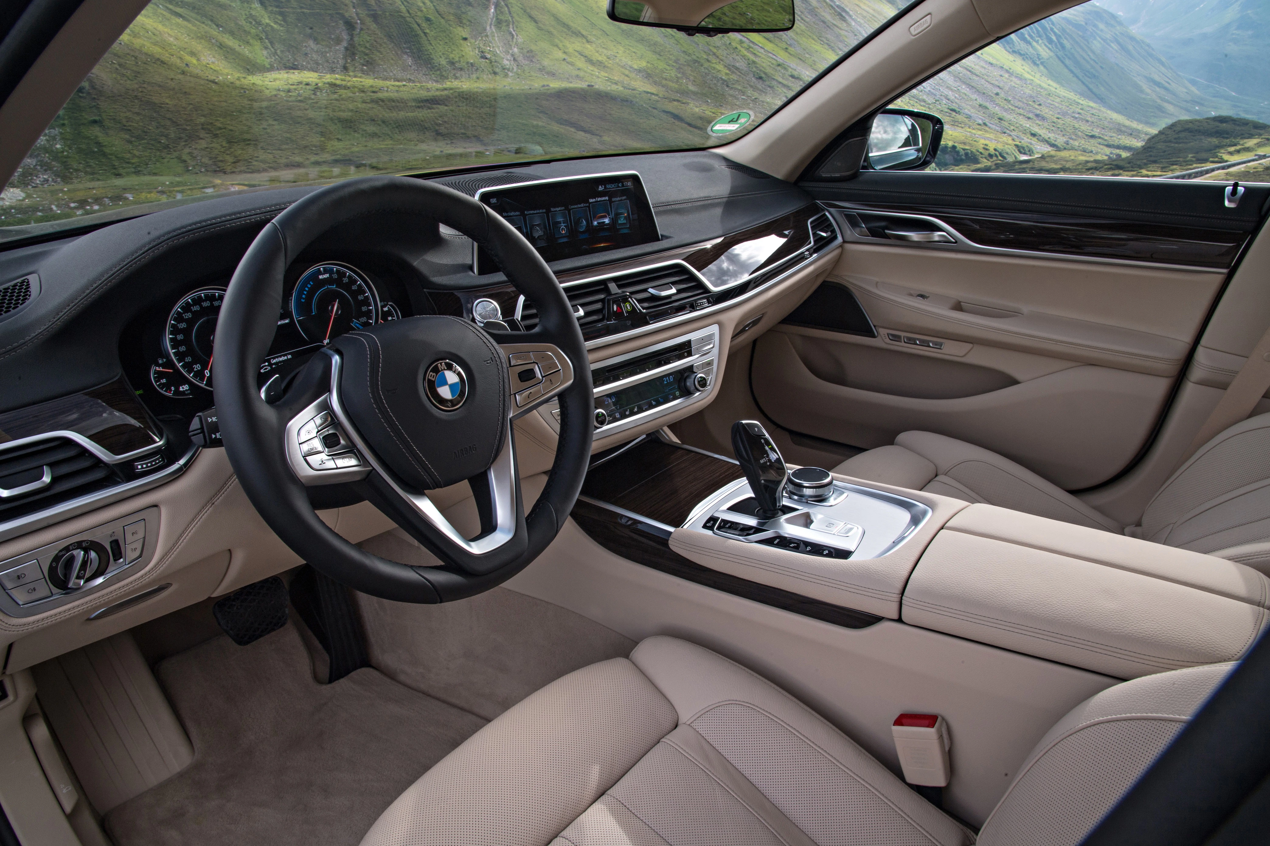Innenraum eines Luxusautos mit beigen Ledersitzen, modernem Armaturenbrett und Lenkrad; Blick auf eine grüne Landschaft durch die Fenster.
