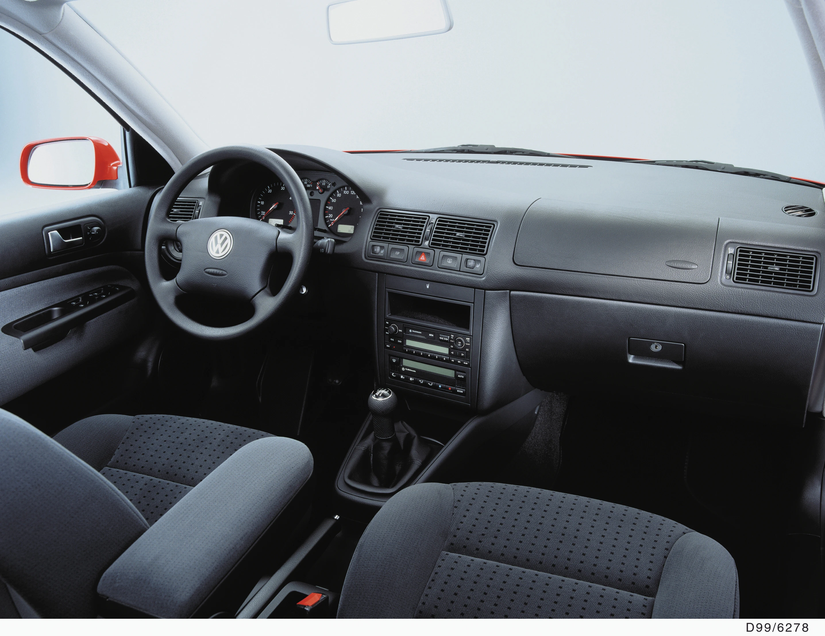 Innenraum eines Autos mit grauen Sitzen, manueller Schaltung und Volkswagen-Emblem auf dem Lenkrad. Moderne Armaturen mit Klimaanlage.