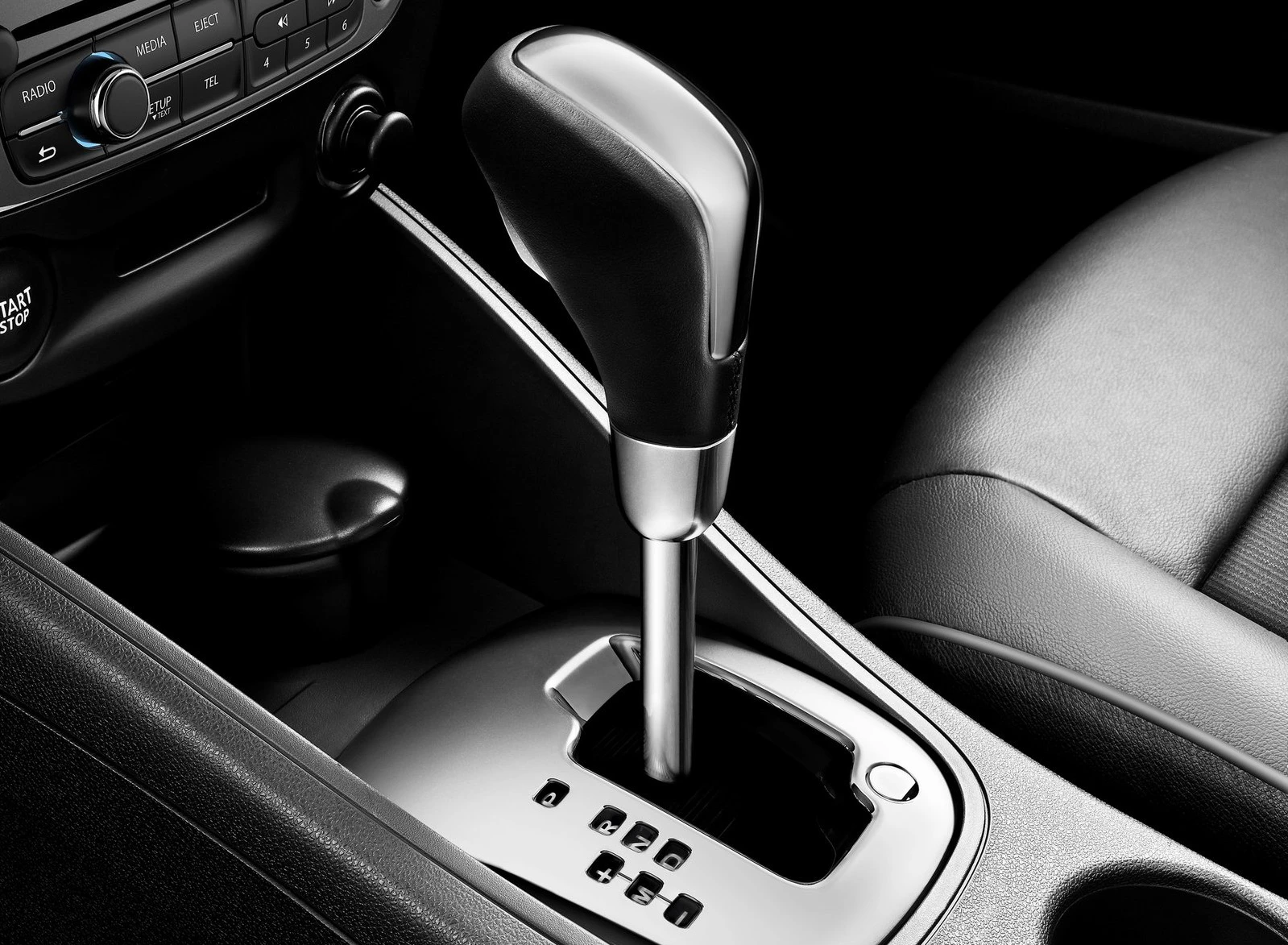 Automatikgetriebe eines Autos in Nahaufnahme, mit schwarzem Schaltknauf und silberner Basis, umgeben von einem schwarzen Innenraum.