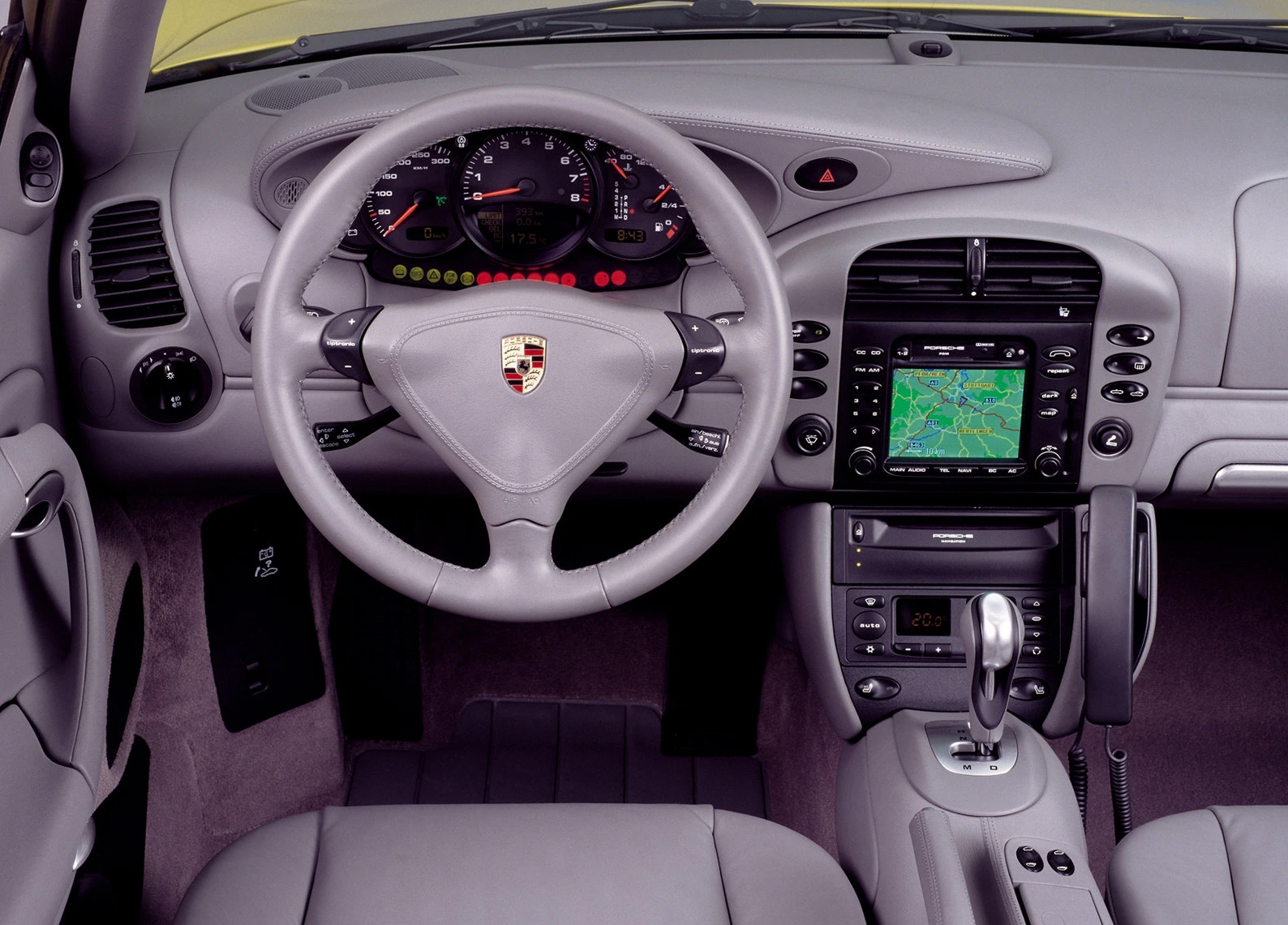 Innenraum eines Autos mit grauem Lenkrad, Tachometer, Navigationseinheit und Mittelkonsole. Modernes Design mit Ledersitzen.