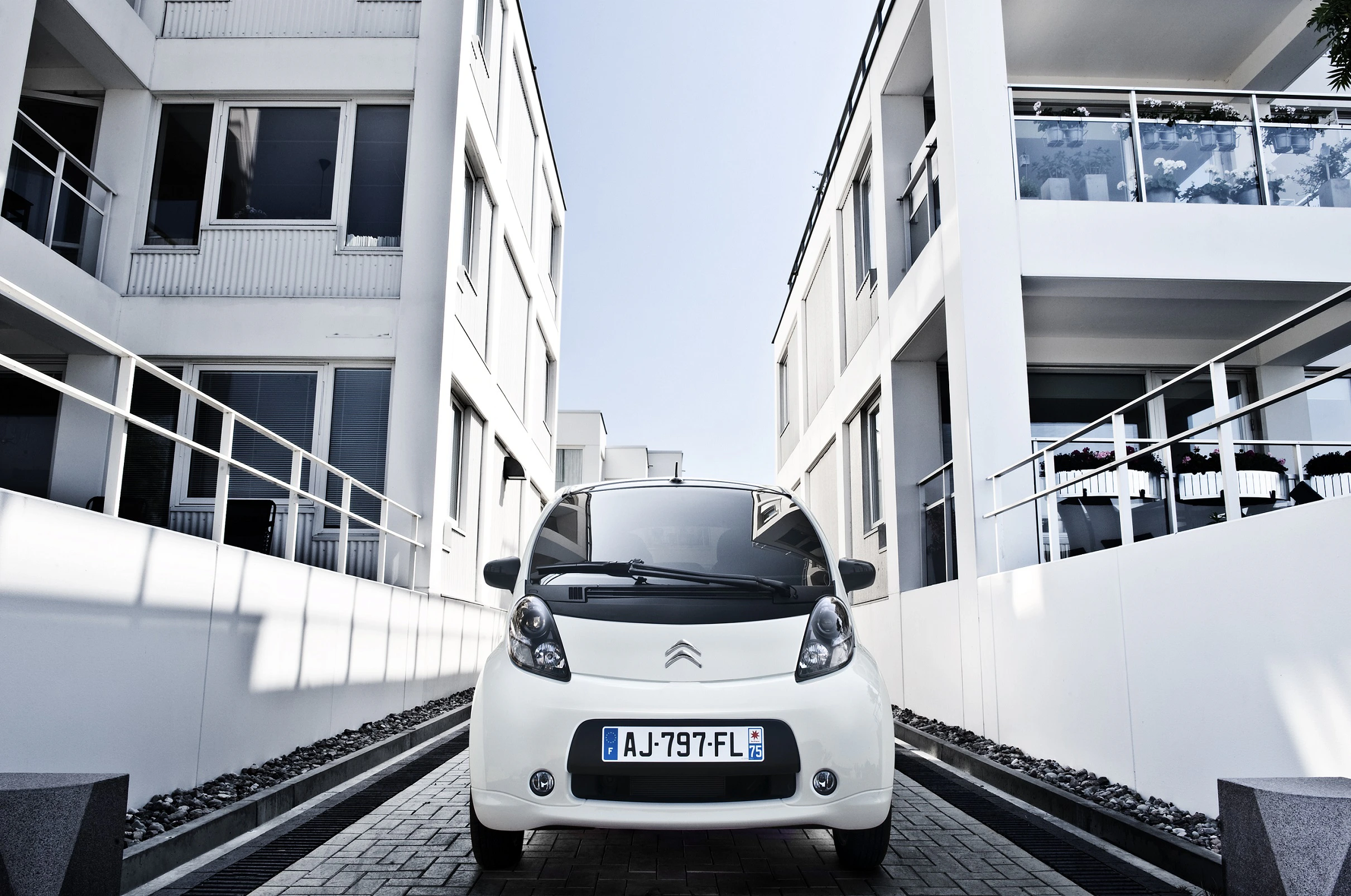 Weißes Auto zwischen modernen Gebäuden, eingefangen aus einer niedrigen Perspektive bei klarem Himmel.