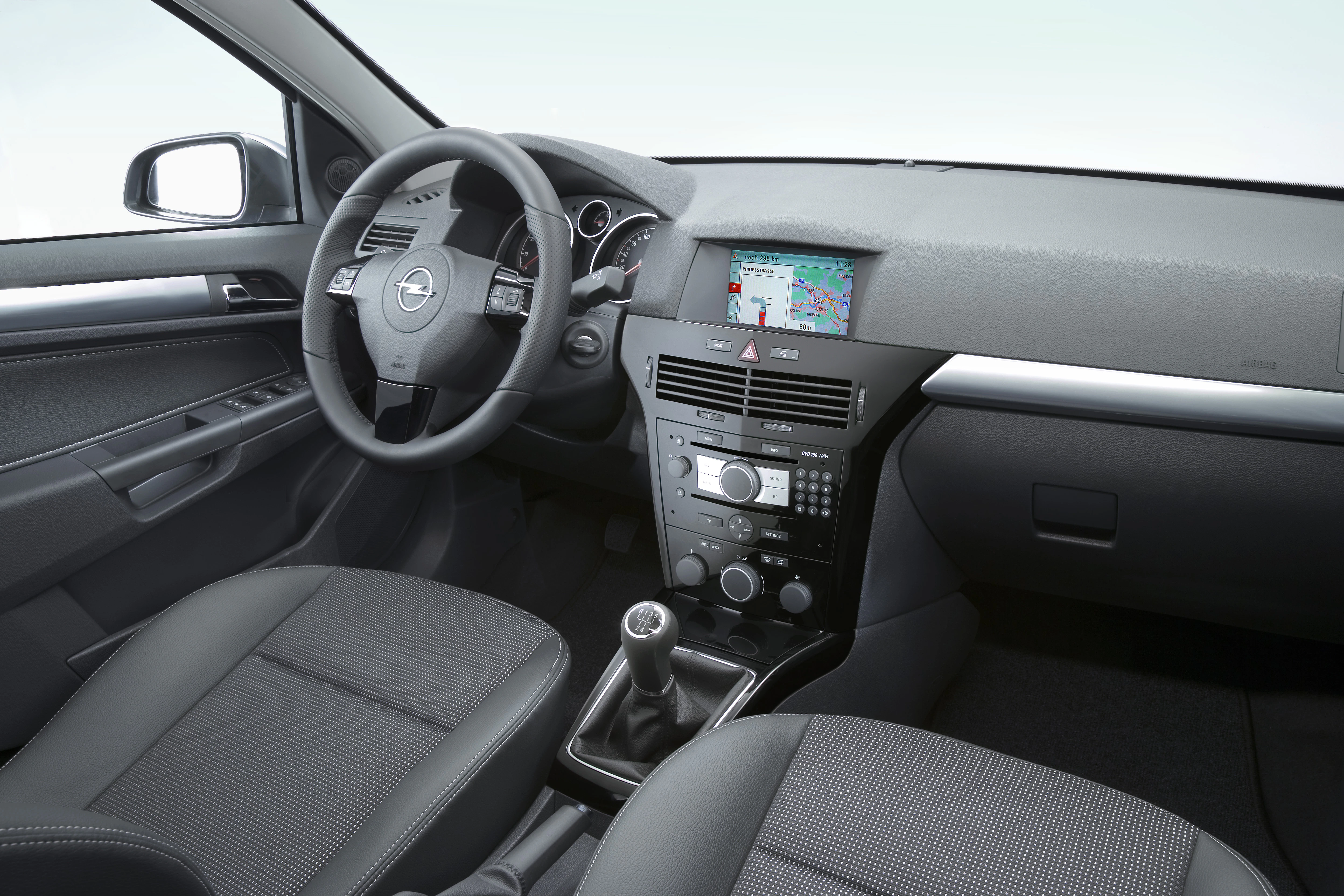 Innenraum eines Autos mit Lenkrad, Schaltknüppel und Navigationssystem. Moderne, graue Ausstattung und klar strukturiertes Armaturenbrett.