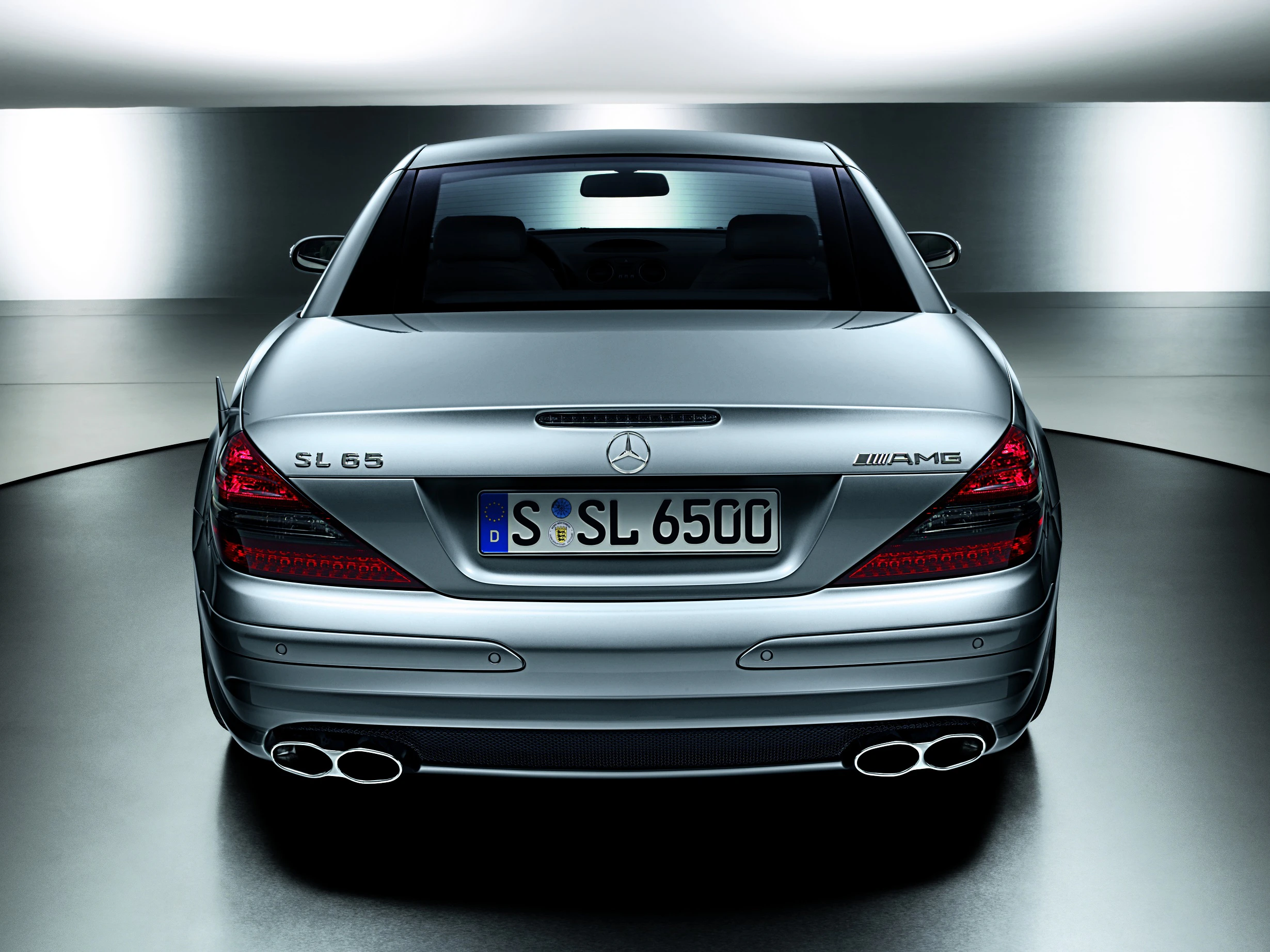 Rückansicht eines silbernen Mercedes-Benz SL 65 AMG mit vier Auspuffrohren und deutschem Kennzeichen in heller Umgebung.