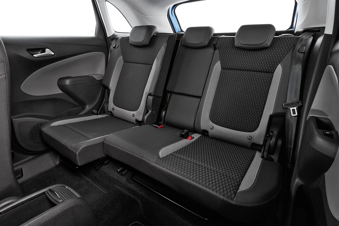 Rückbank eines Autos mit grauen, gemusterten Sitzbezügen, schwarzen Kopfstützen und heller Innenverkleidung.