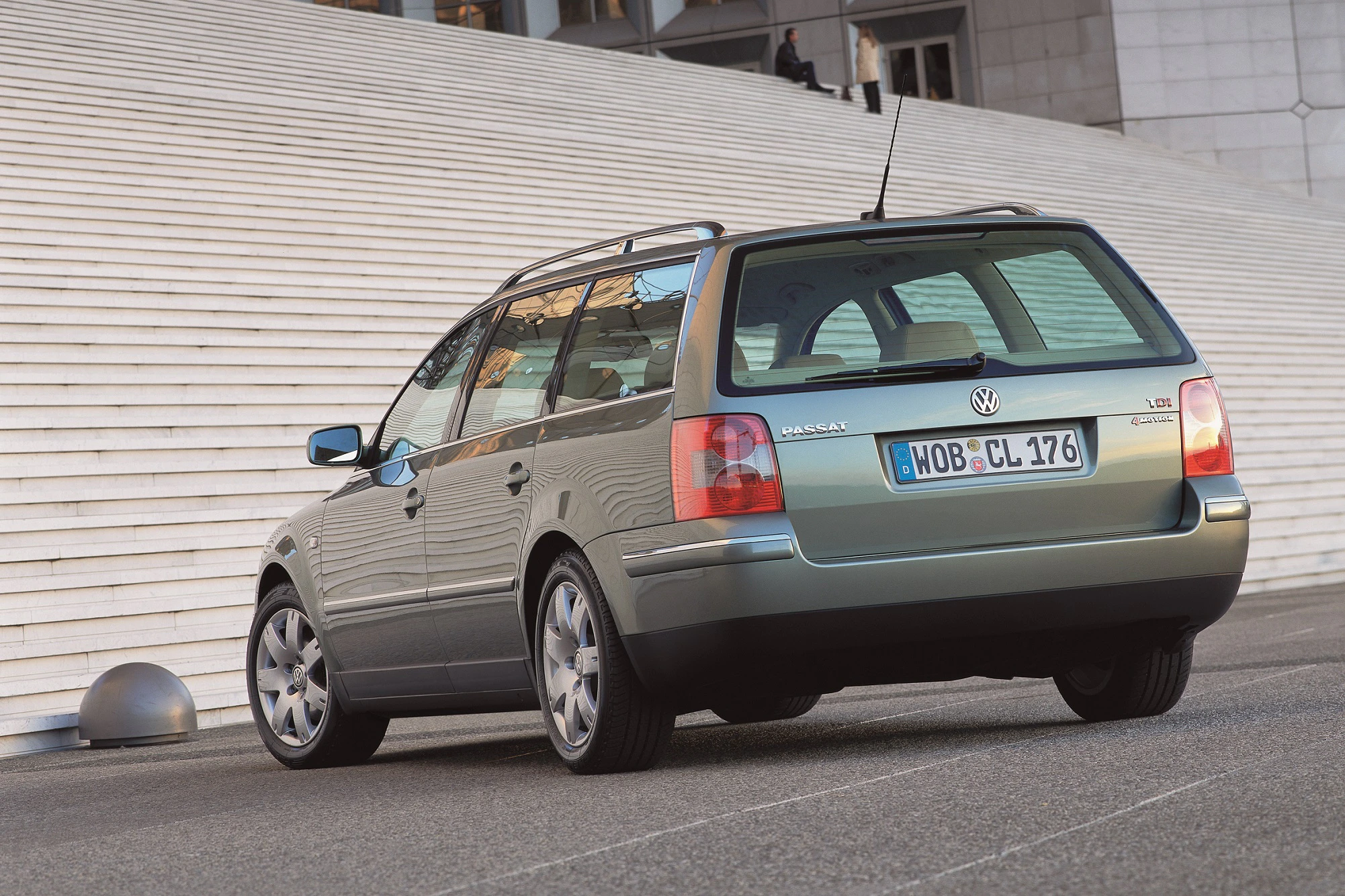 Grüner Volkswagen Kombi vor einer großen Treppe geparkt, Hecktür geschlossen, klarer Himmel, am Tag aufgenommen.