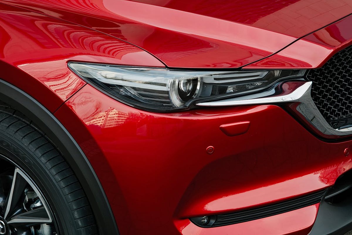 Nahaufnahme eines roten Autos, das einen Abschnitt der Frontpartie mit Scheinwerfer und markantem Kühlergrill zeigt.