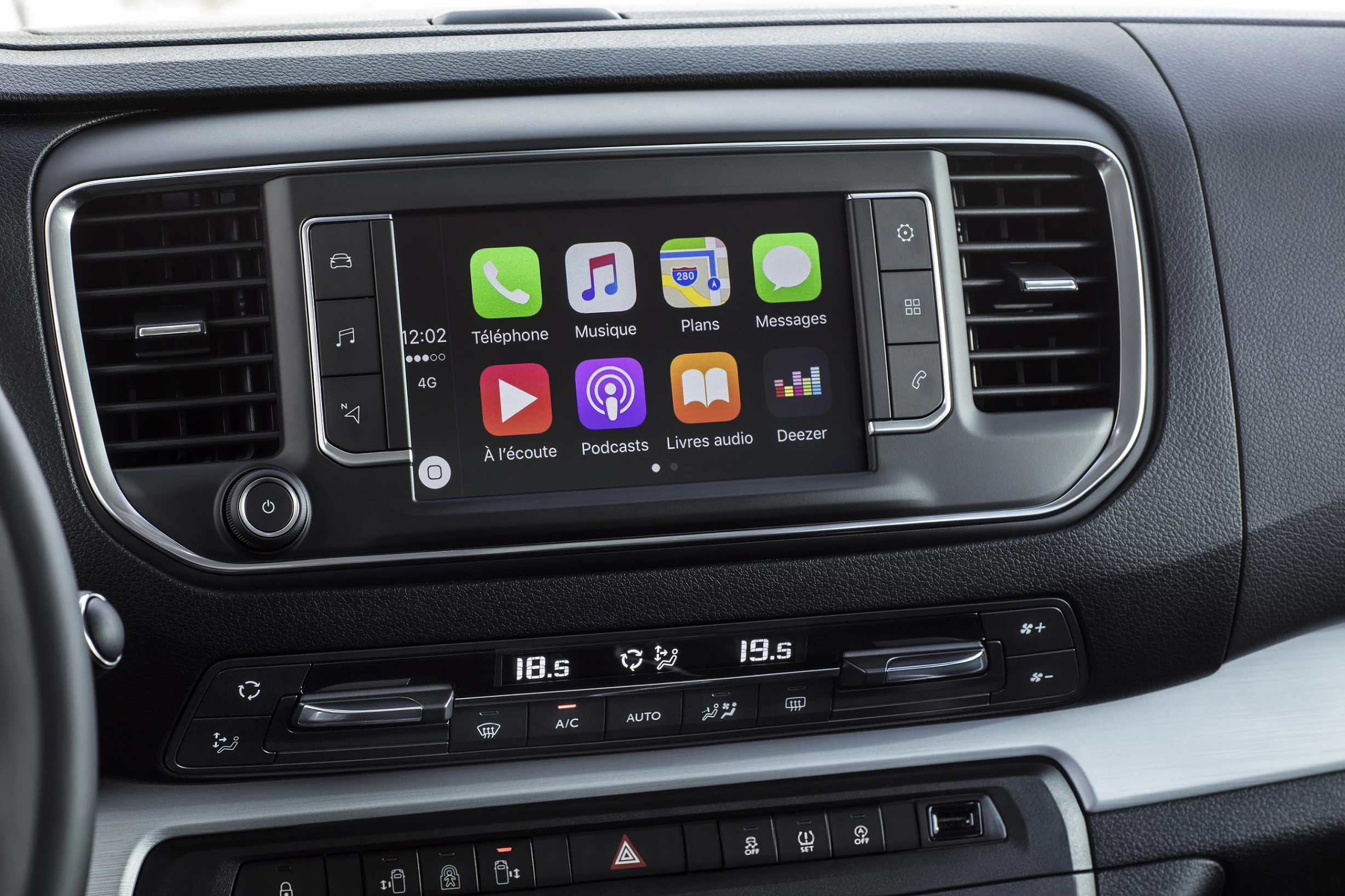 Autoinnenraum mit Touchscreen-Display, das App-Symbole wie Telefon, Musik und Karten zeigt. Darunter ist die Klimaanlagensteuerung.