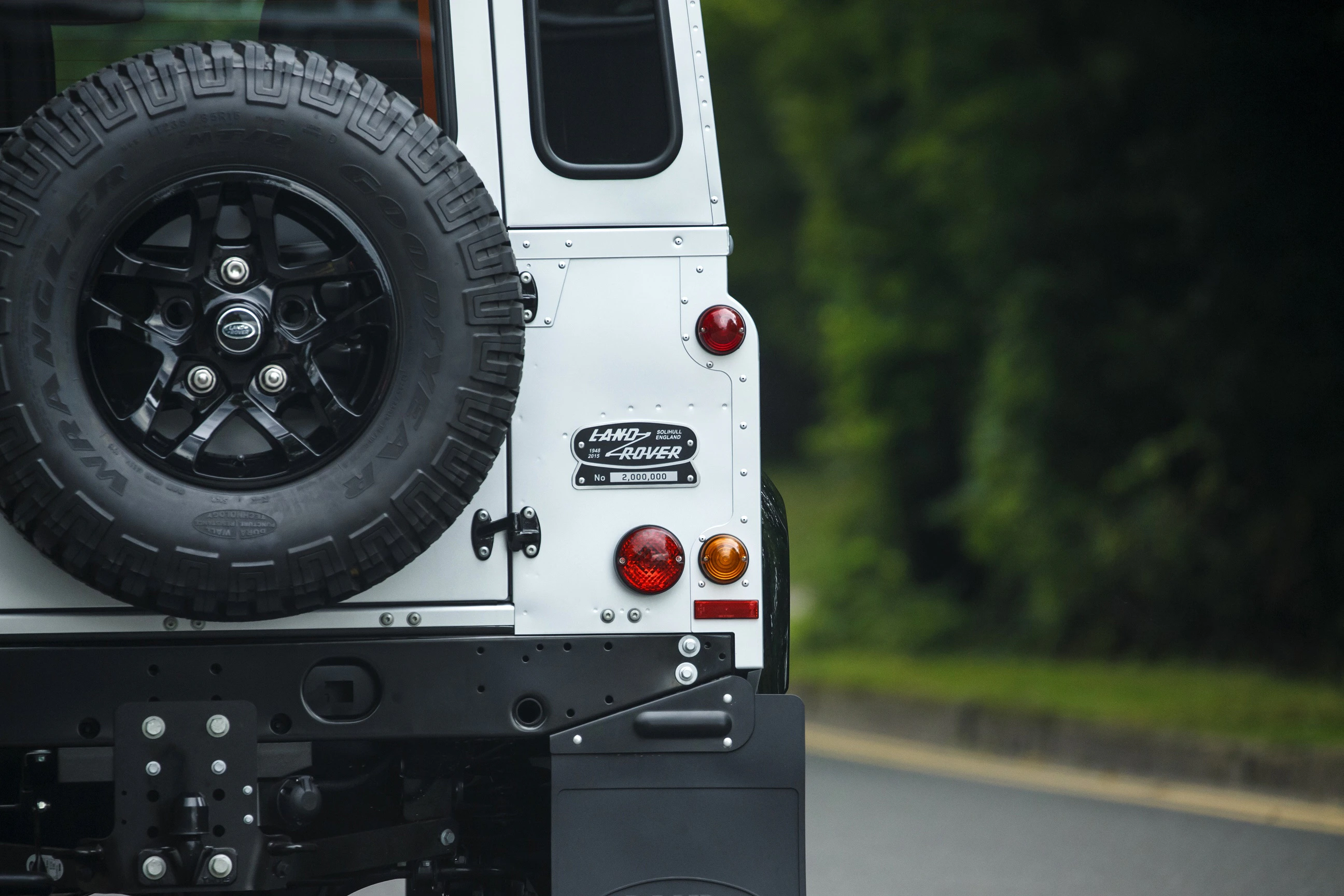 Teil eines weißen Geländewagens mit Reserverad und Land Rover-Logo, geparkt auf einer straße nahe einem grünen Wald.