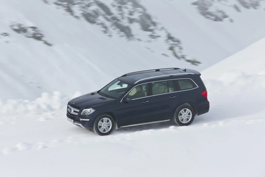 Ein schwarzer SUV fährt auf einer verschneiten Bergstraße bergauf, umgeben von schneebedeckten Bergen und klarem Himmel.