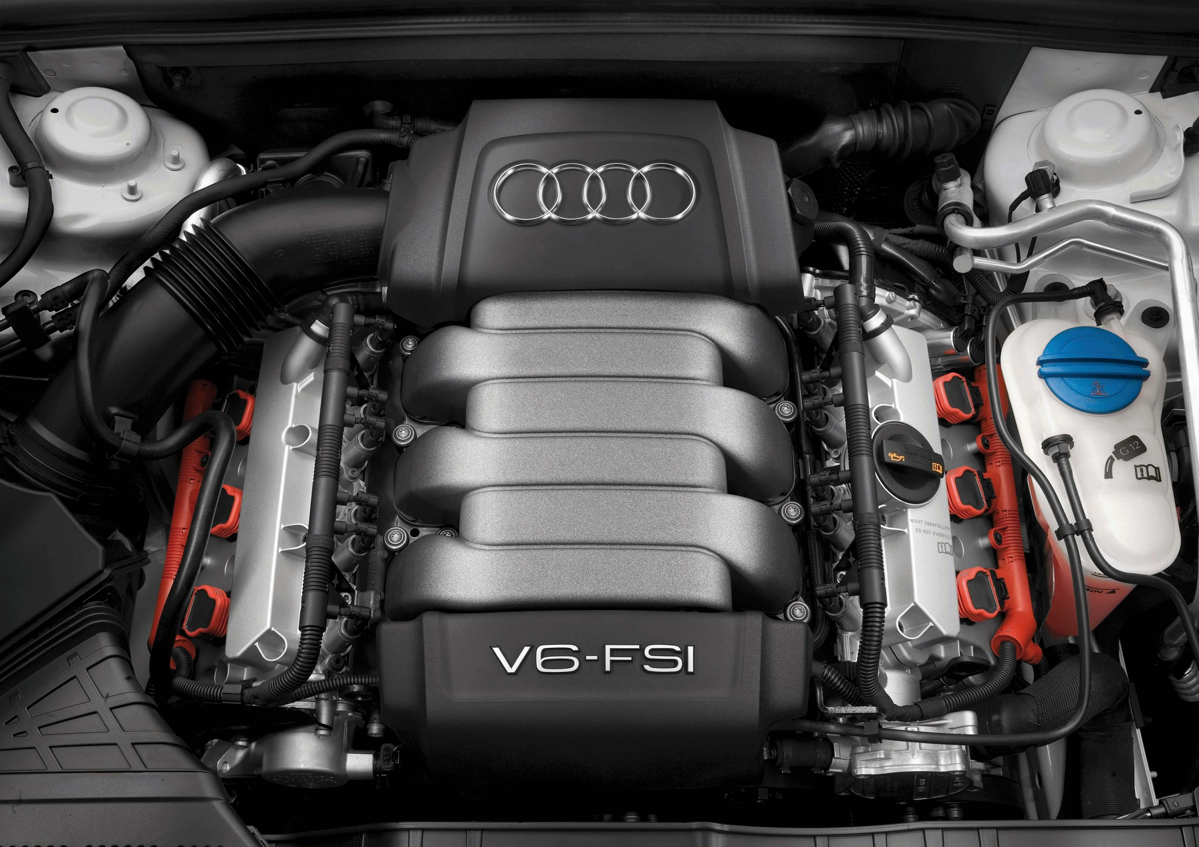 Nahaufnahme eines V6-FSI-Motors in einem Audi-Fahrzeug. Sichtbar sind die Abdeckung mit Audi-Logo und technische Komponenten.