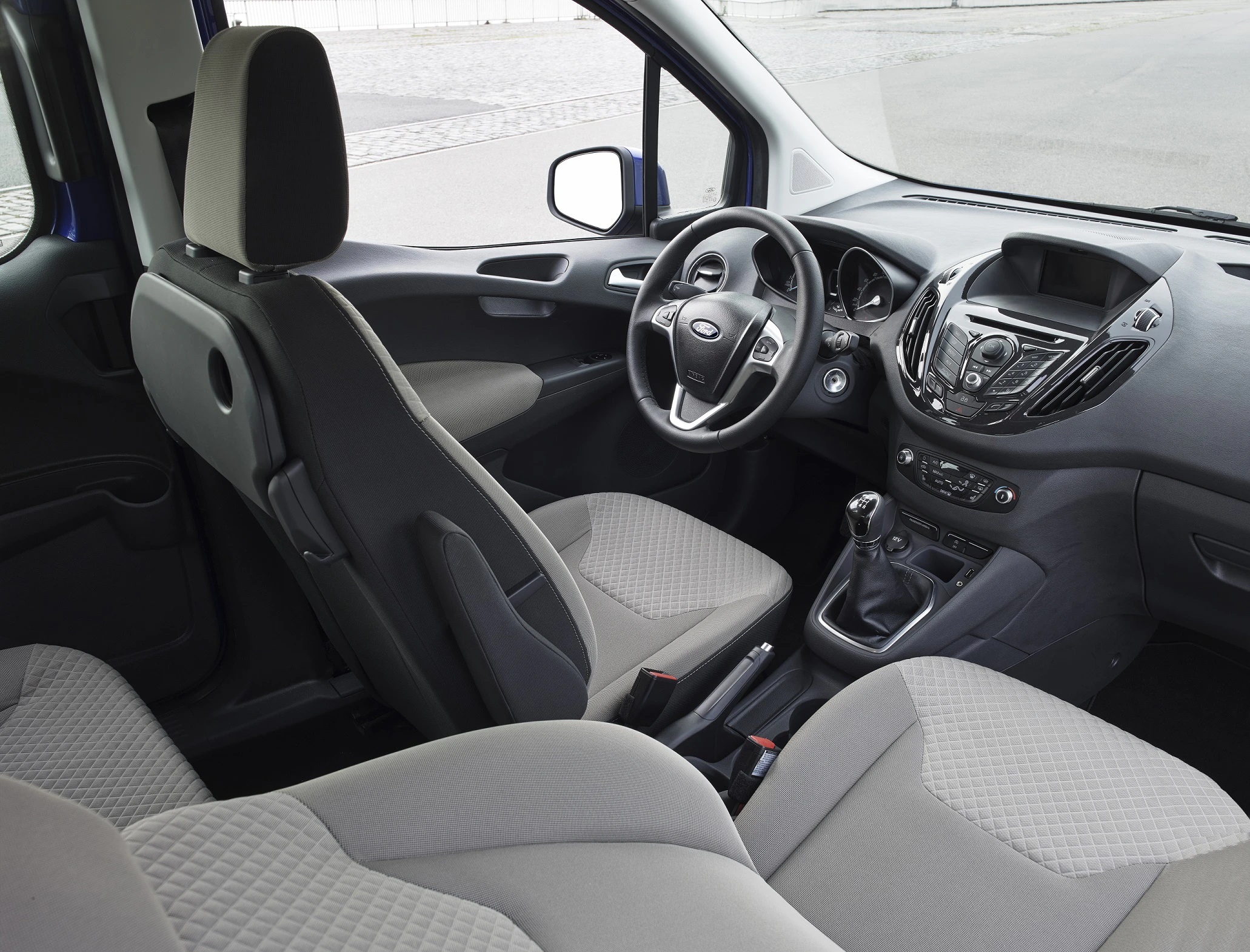 Innenraum eines Autos mit grauen Stoffpolstern, Lenkrad, Schalthebel und moderner Instrumententafel. Sicht vom Rücksitz nach vorne.