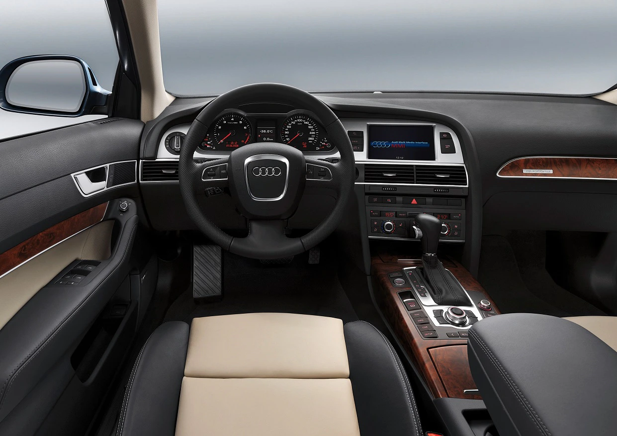 Innenraum eines Audi-Fahrzeugs mit Lederlenkrad, Armaturenbrett mit digitalen Anzeigen, Holzverkleidung und Multimedia-Bildschirm.