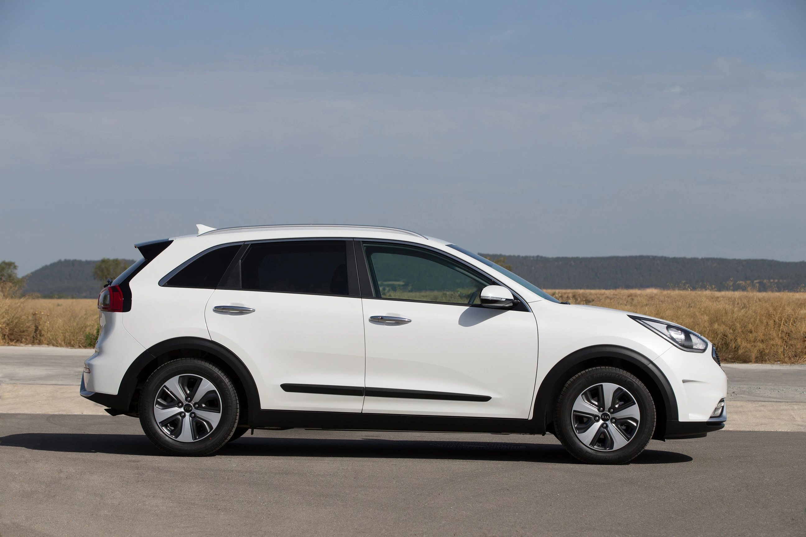 Weißer SUV parkt seitlich auf asphaltiertem Untergrund mit blauer Himmel und braunem Feld im Hintergrund.