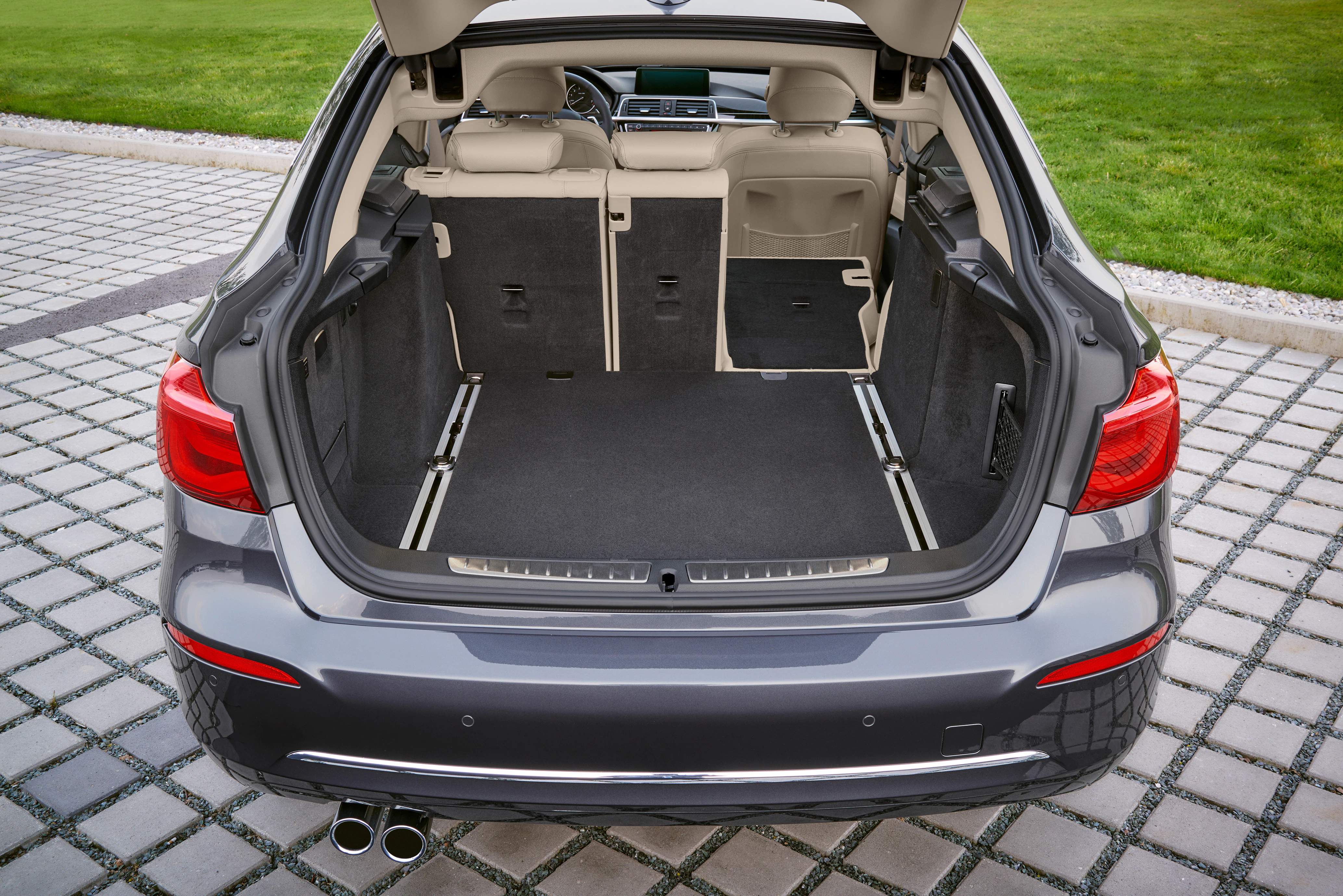 Rückansicht eines geöffneten Kofferraums eines silbernen Autos, das auf gepflastertem Boden geparkt ist. Die Rücksitze sind teilweise umgeklappt.