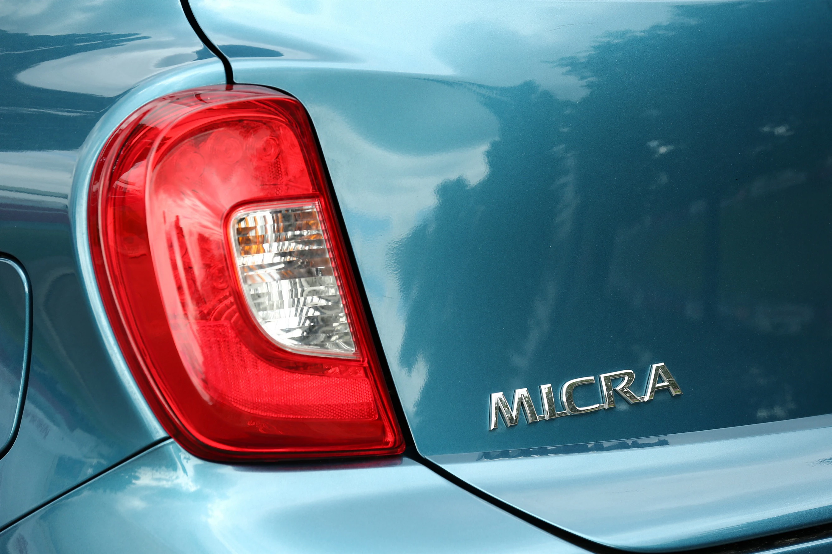Nahaufnahme eines blauen Autos mit rotem Rücklicht und dem Schriftzug "MICRA" auf der Heckklappe.