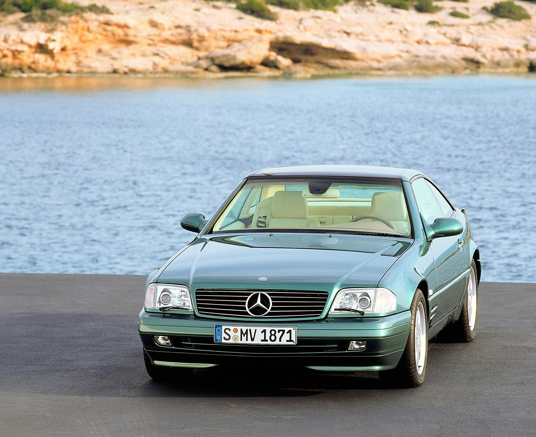 Ein grüner Mercedes-Benz Coupé steht auf Asphalt vor einer Meereskulisse mit felsigem Ufer im Hintergrund.