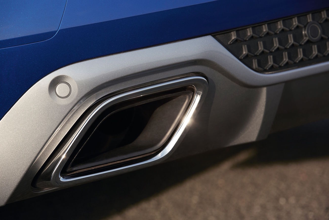 Nahaufnahme eines rechteckigen Autoauspuffs mit silberner Umrandung an einem blauen Fahrzeug, daneben Wabenmuster und Sensor.