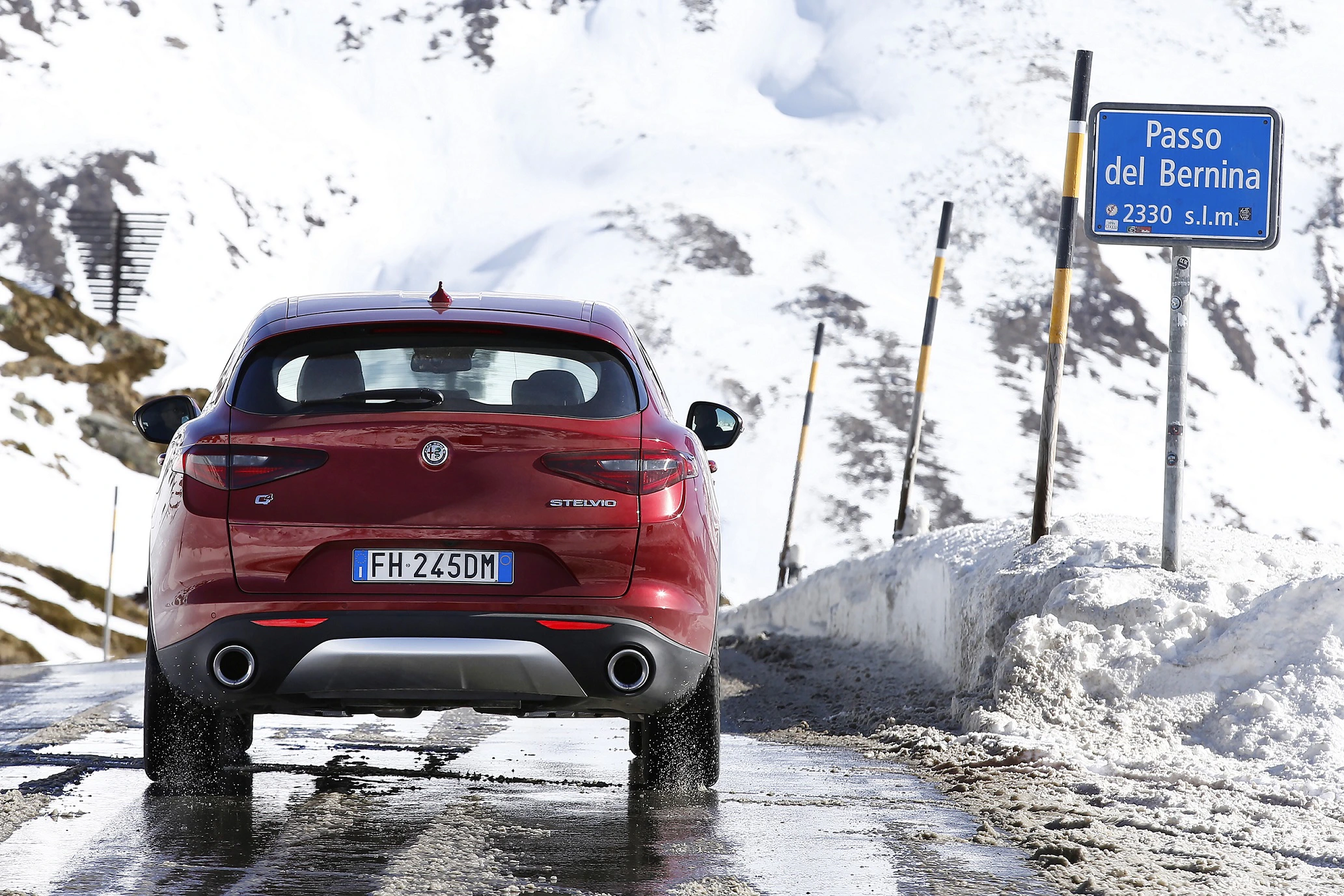 Ein rotes Auto fährt auf einer verschneiten Straße am Passo del Bernina vorbei. Ein blaues Schild zeigt die Höhe von 2330 m an.