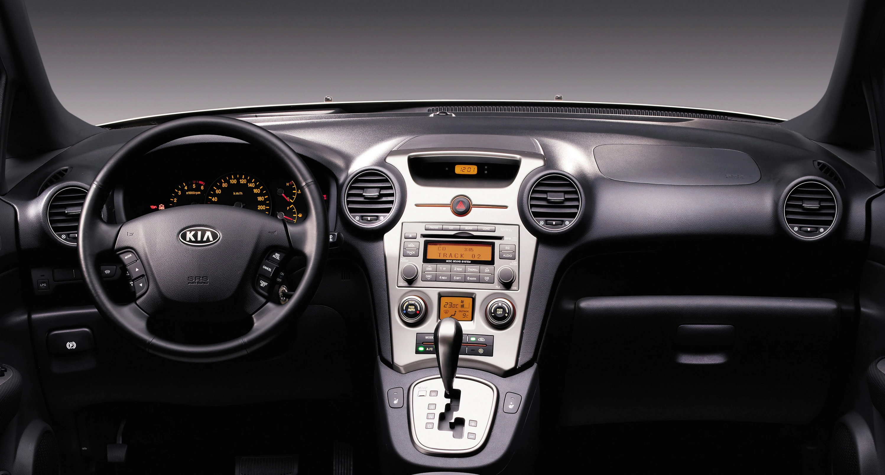 Innenraum eines Autos mit Kia-Logo auf dem Lenkrad, Mittelkonsole mit Steuerungen und Lüftungsschlitzen, Automatikgetriebehebel sichtbar.
