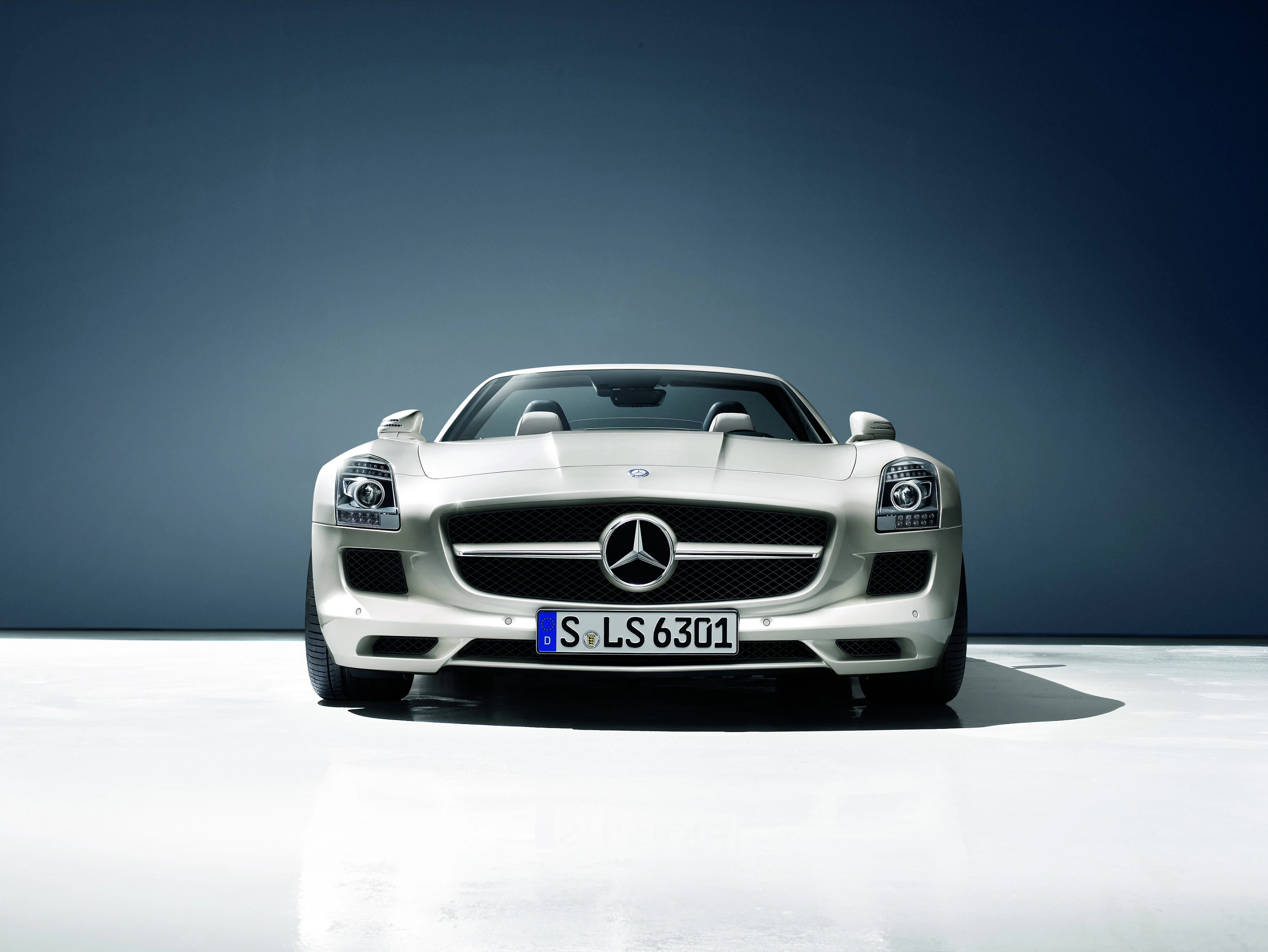 Silberner Sportwagen, Mercedes-Benz, mit markantem Kühlergrill und Scheinwerfern, steht vor minimalistischem, dunklem Hintergrund.