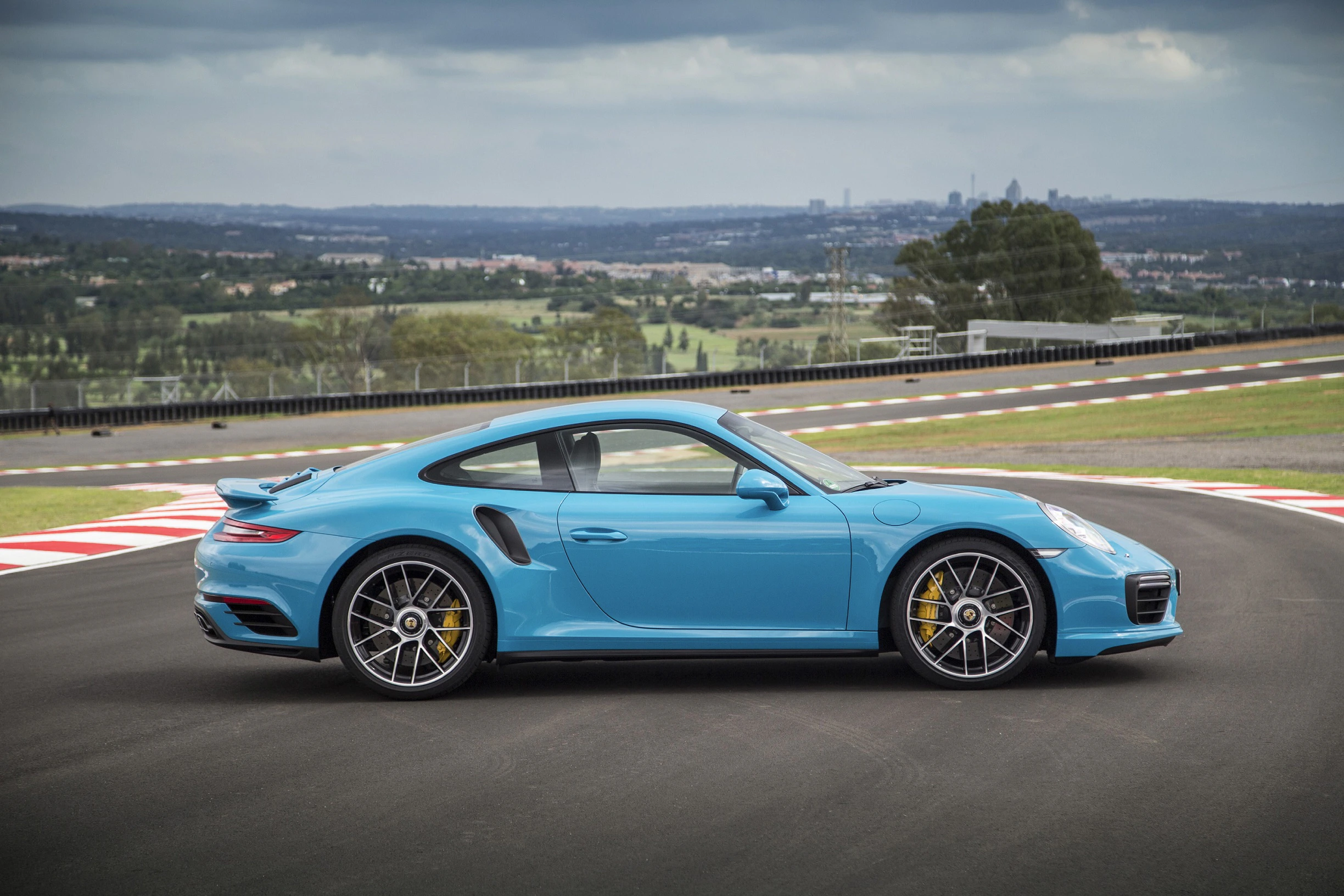 Blauer Sportwagen auf einer Rennstrecke vor einer Panoramaansicht; seitliche Perspektive zeigt dynamisches, modernes Design.