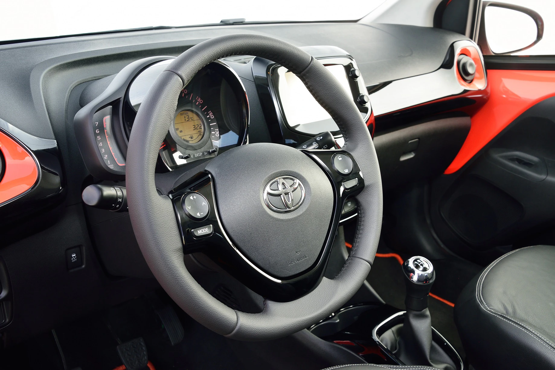 Innenraum eines Autos mit Lenkrad, Schalthebel und Armaturenbrett. Moderne Anzeige und rote Akzente verleihen dem Interieur einen sportlichen Look.