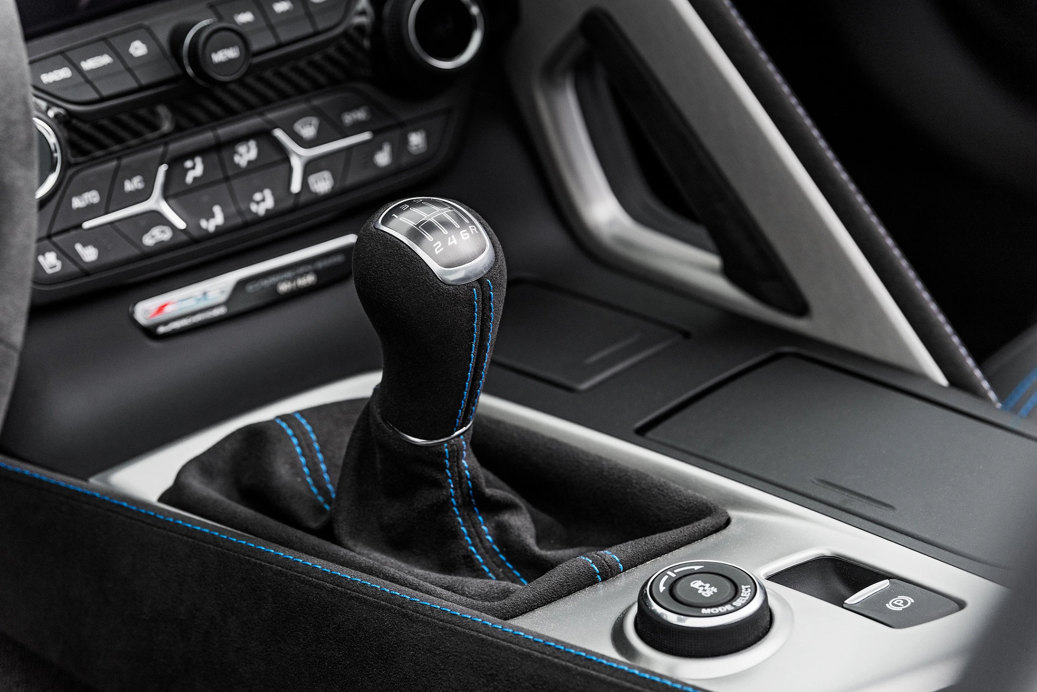 Gangschaltung und Armaturenbrett eines Autos mit schwarzem Leder und blauen Nähten, umgeben von verschiedenen Bedienelementen.