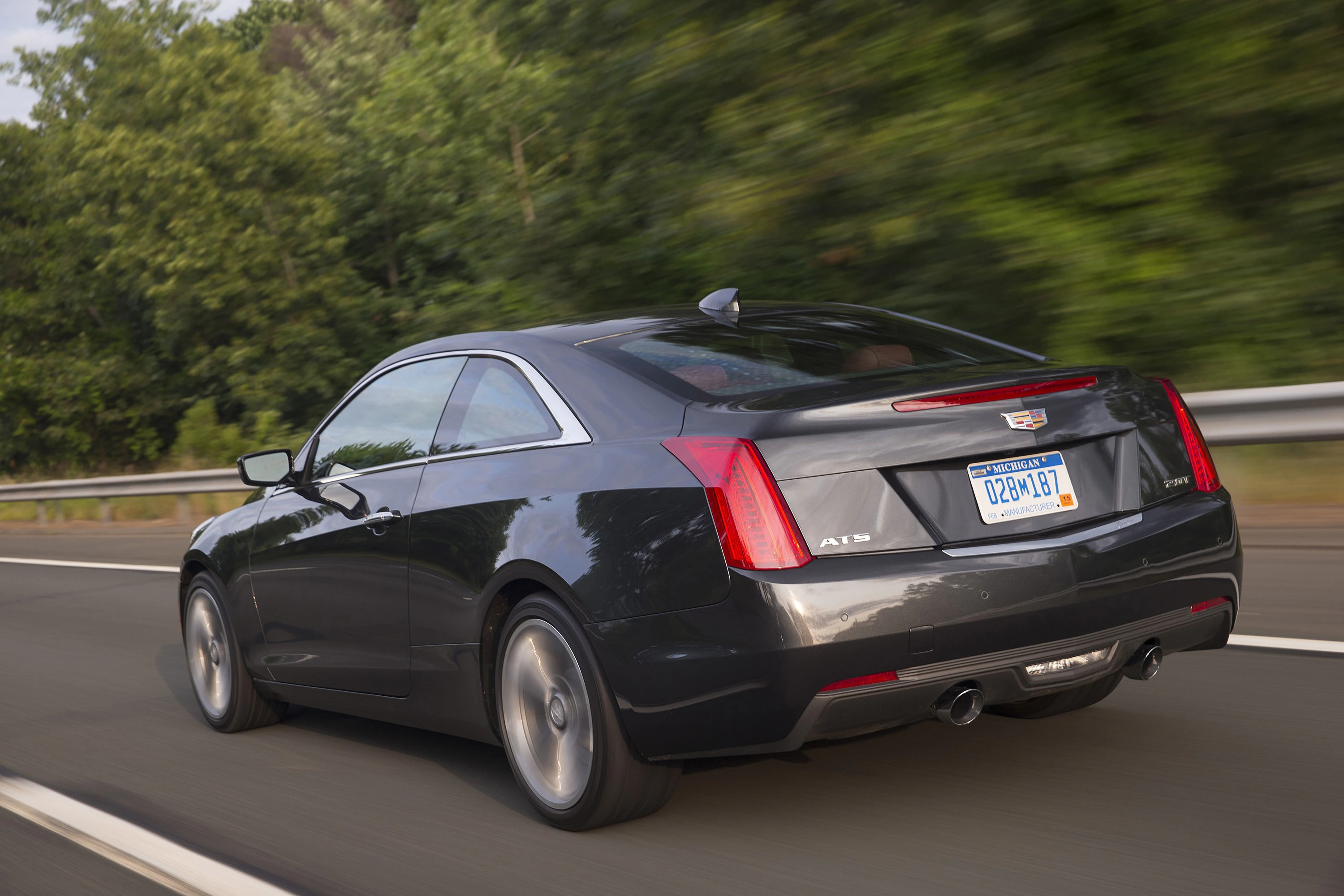 Schwarzer Cadillac ATS Coupé fährt auf einer Landstraße mit Bäumen im Hintergrund.
